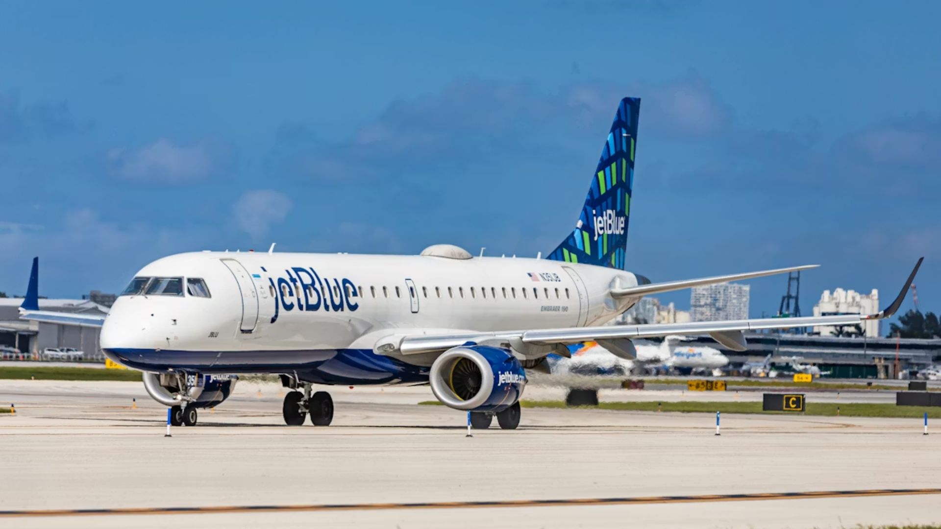 A JetBlue airplane on an airport runway under a clear blue sky.