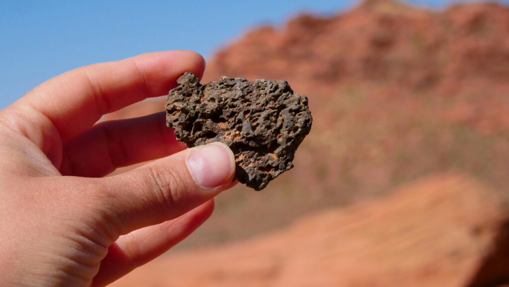 Hand holding a porous dark rock against a desert landscape.