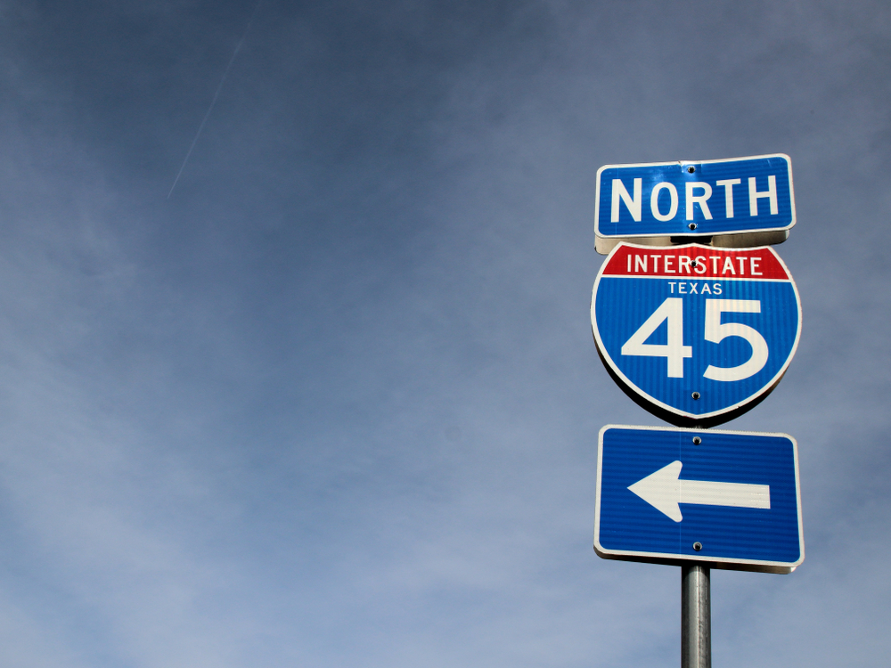 Northbound Interstate 45 Texas highway sign with a left arrow against a slightly dark blue sky.