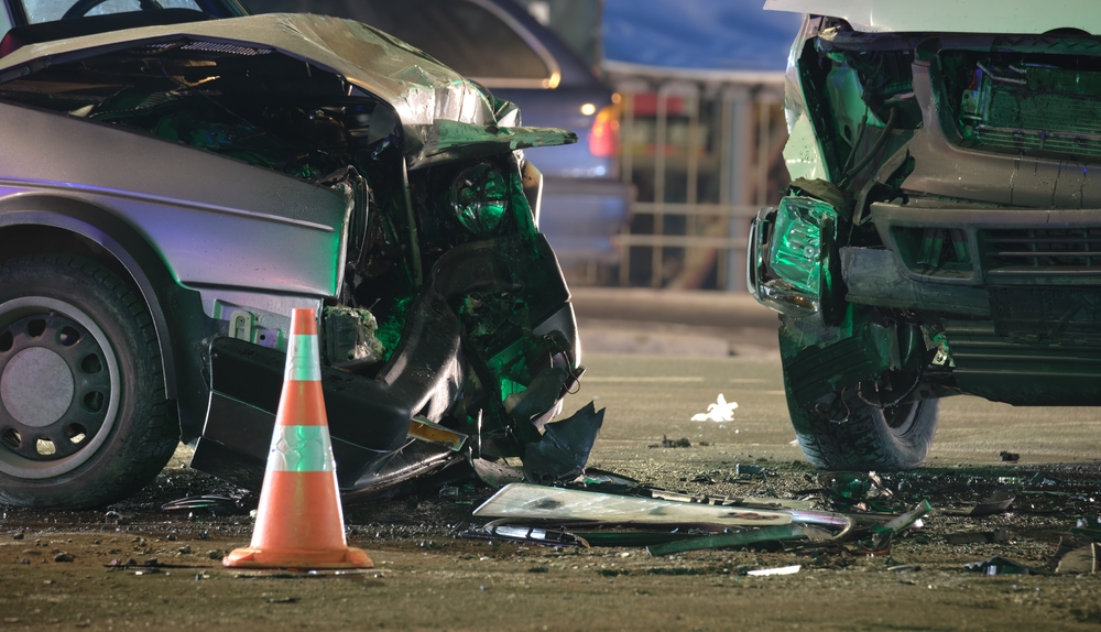 Two heavily damaged cars after a collision with debris scattered on the road at night.