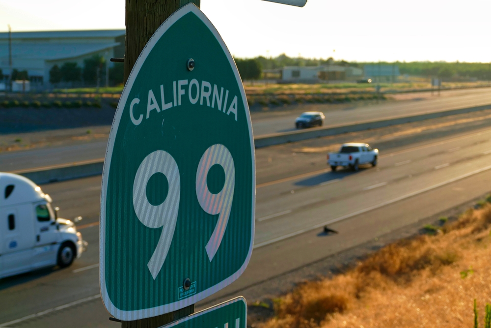 California Route 99 highway sign beside a multi-lane freeway with cars driving in the background.