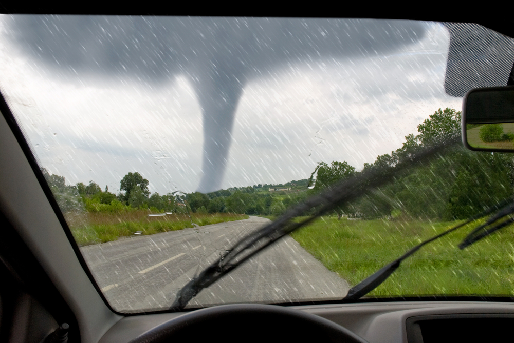 Tornado forming over a rural road seen through a car windshield during heavy rain.