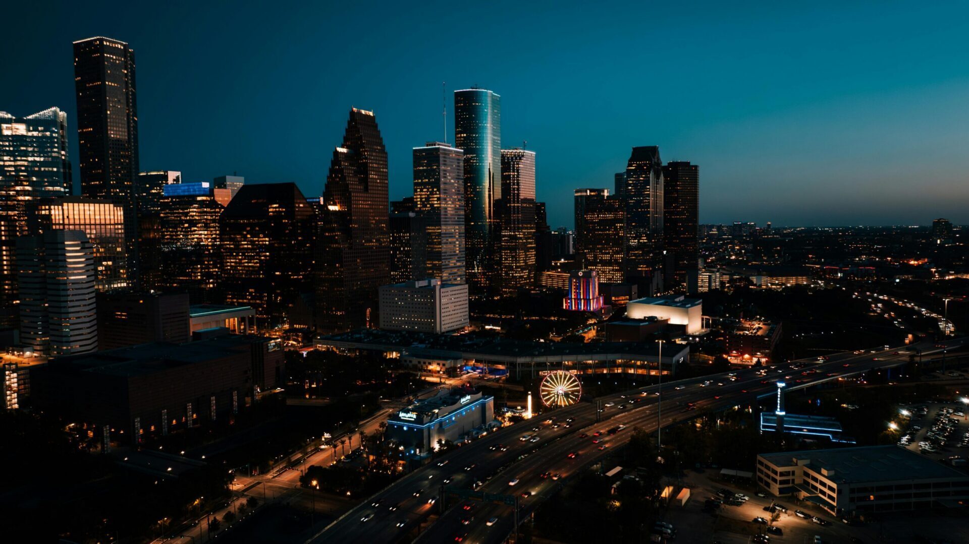 City skyline at night with illuminated buildings and traffic lights in a downtown urban area.