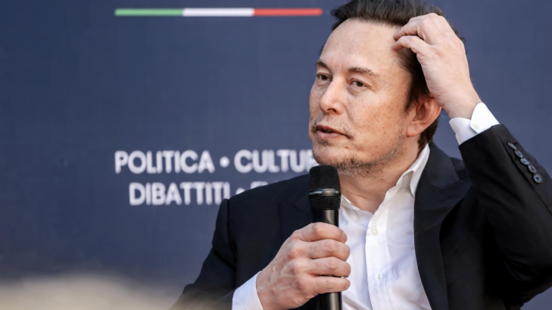 Image 1 Alt Text: A close-up of Elon Musk speaking into a microphone at an event.