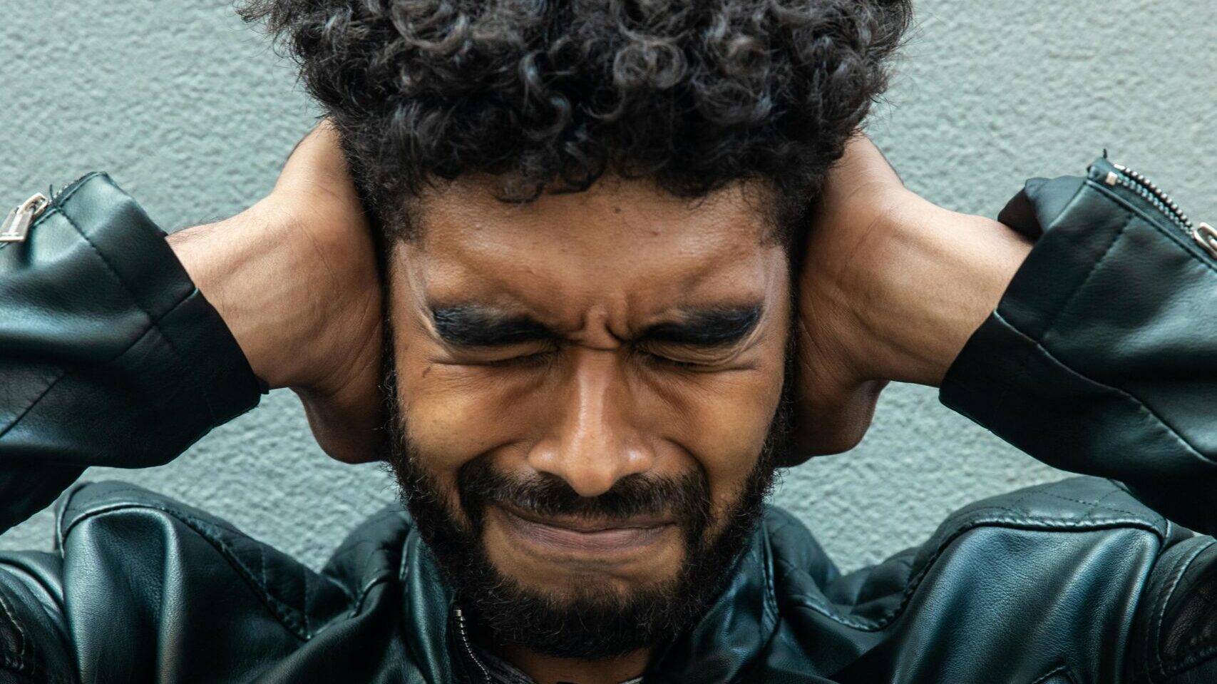 Man covering his ears in distress while sitting indoors.