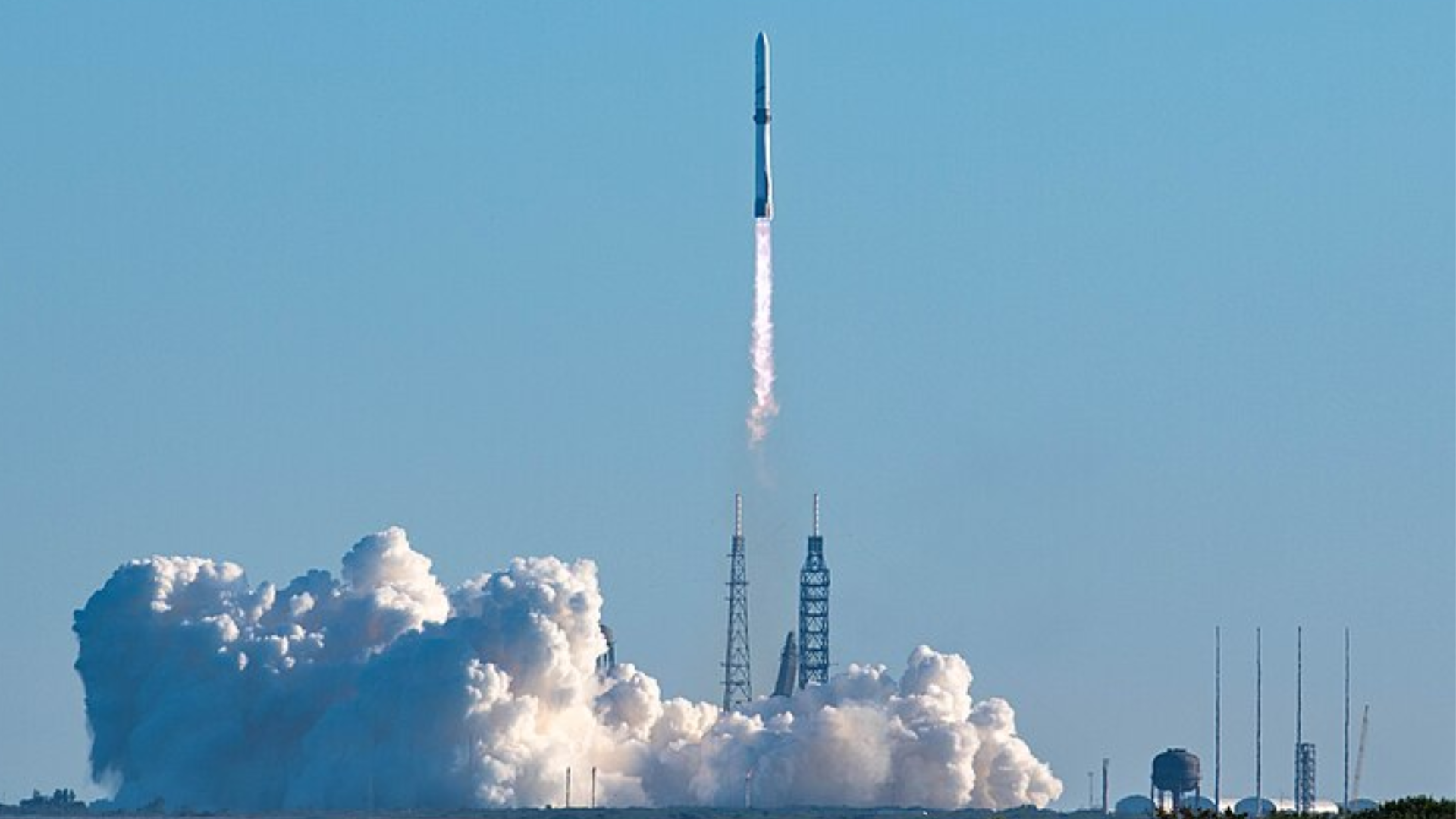 A white rocket launching into a clear blue sky, leaving a large cloud of white smoke on the ground.