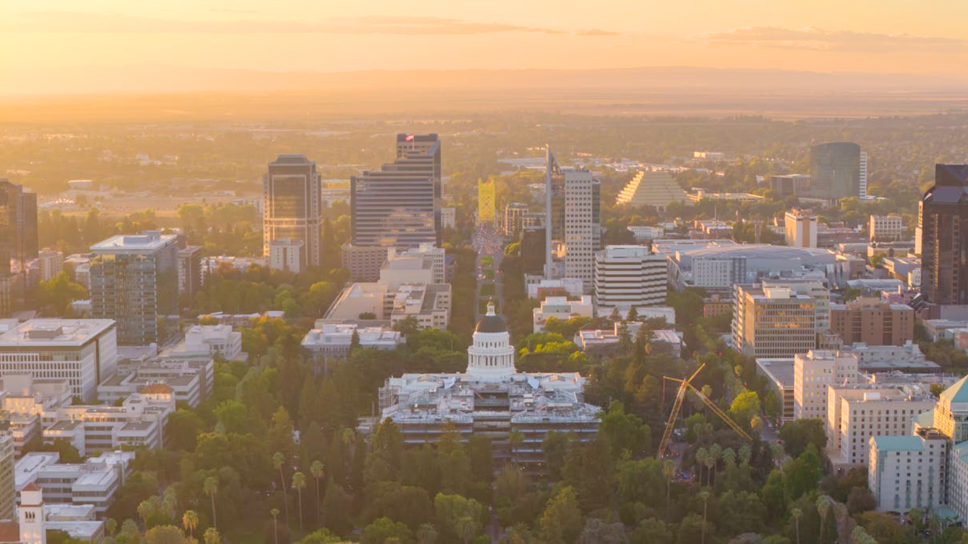 An aerial view of a city skyline with a large white domed building glowing at sunset.