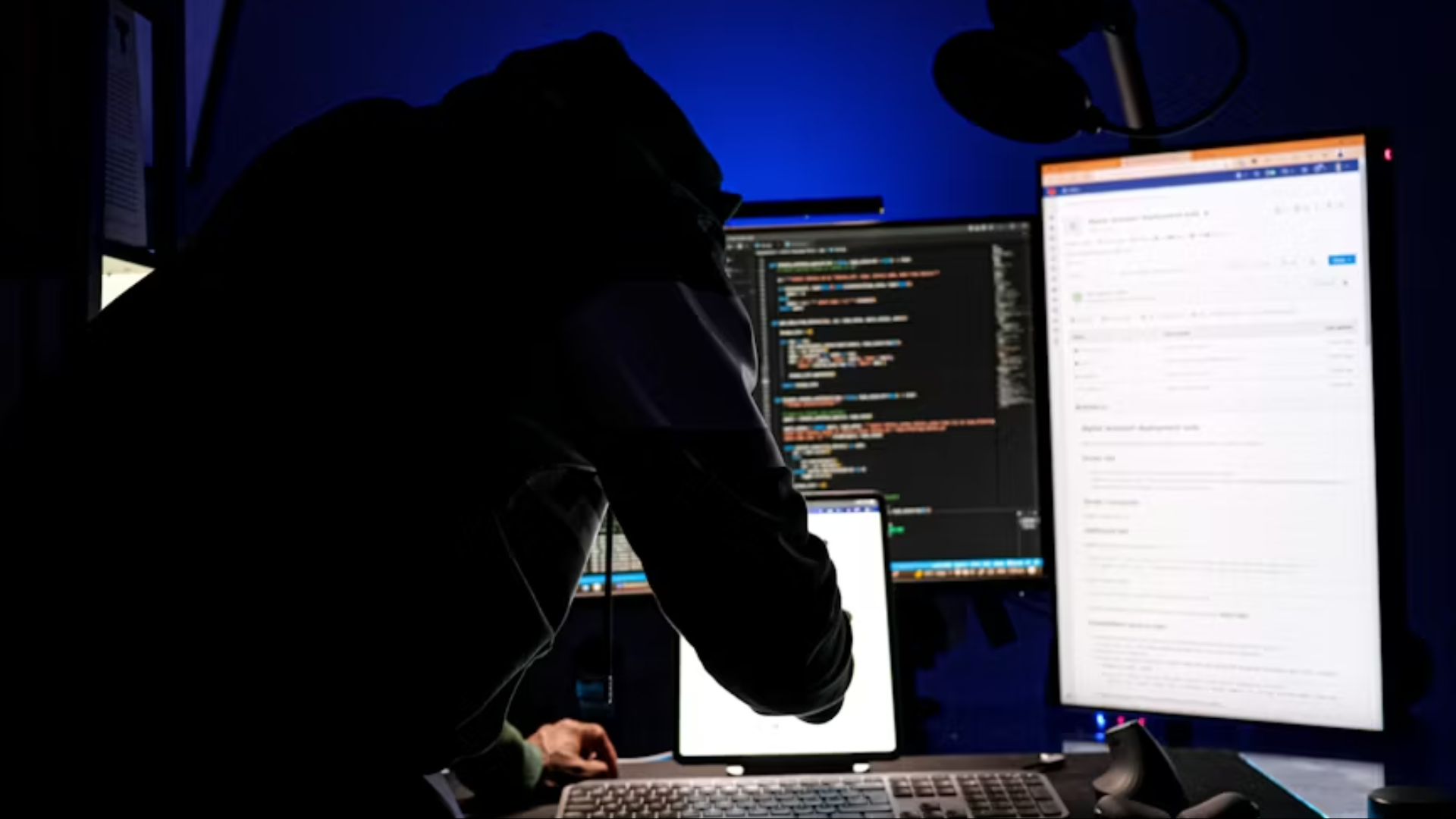 Person in dark room working at multiple monitors displaying code on a computer setup.
