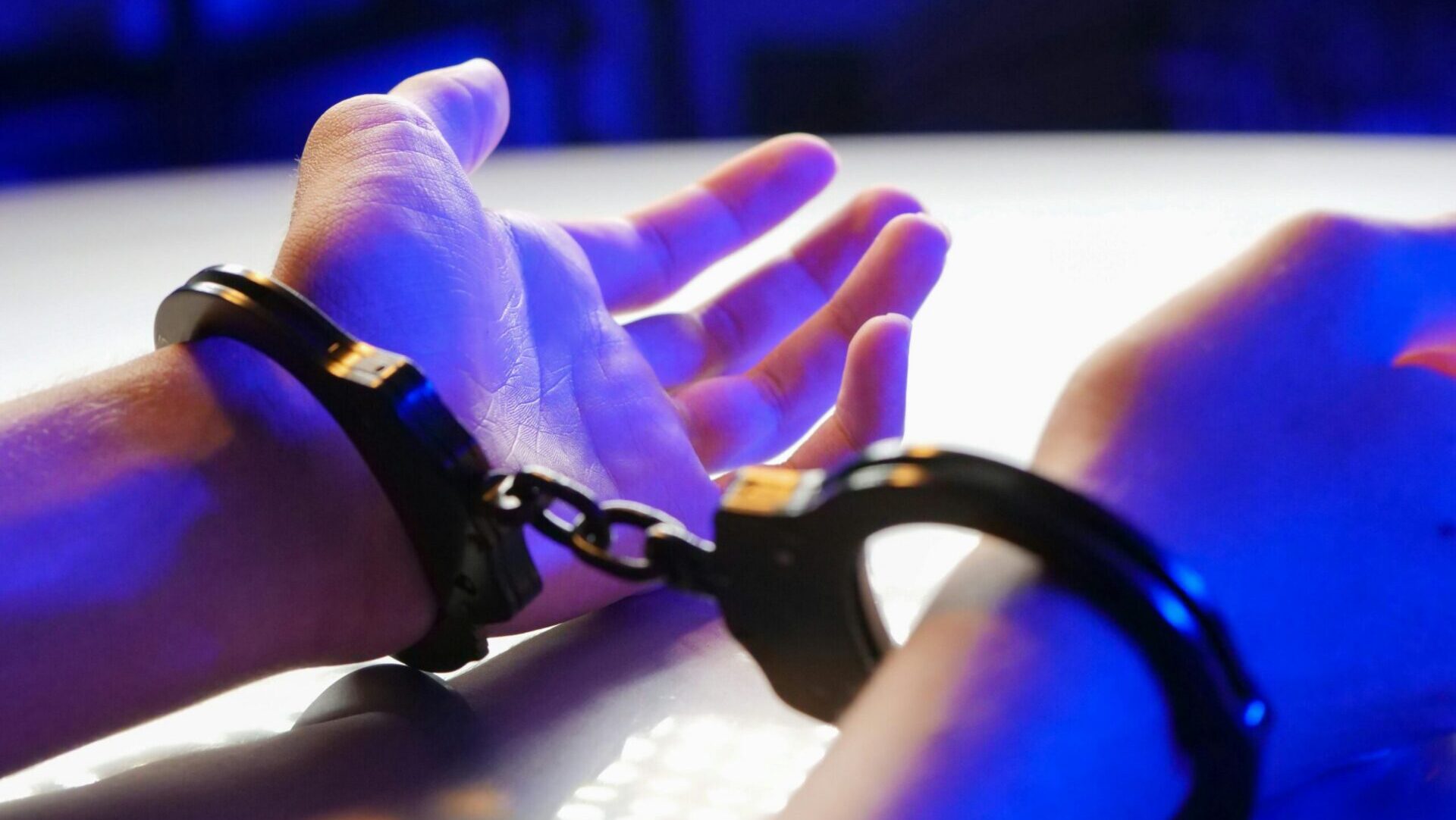 Person in handcuffs with hands behind back under blue lighting.