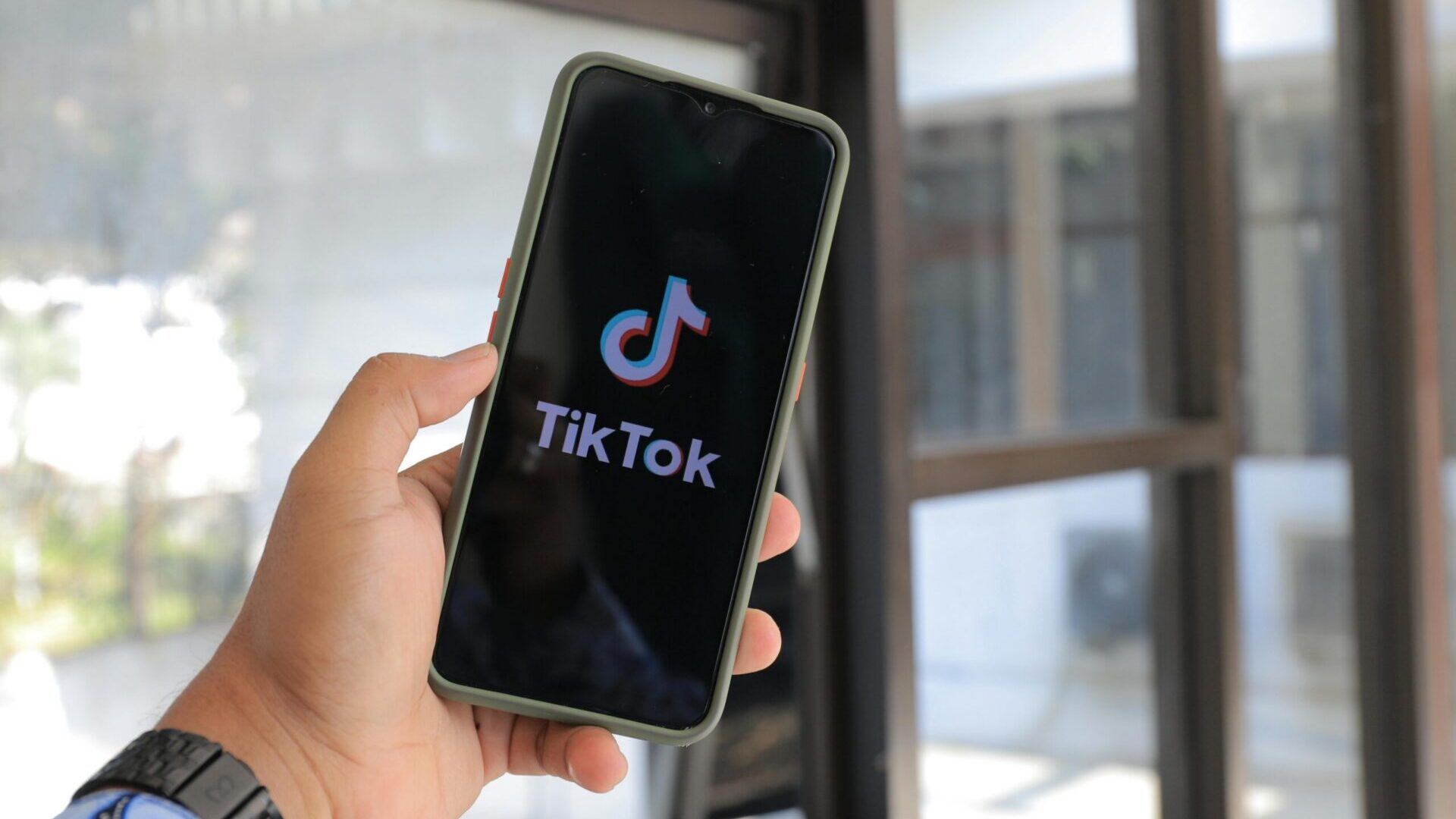 Hand holding a smartphone displaying the TikTok app logo on screen.