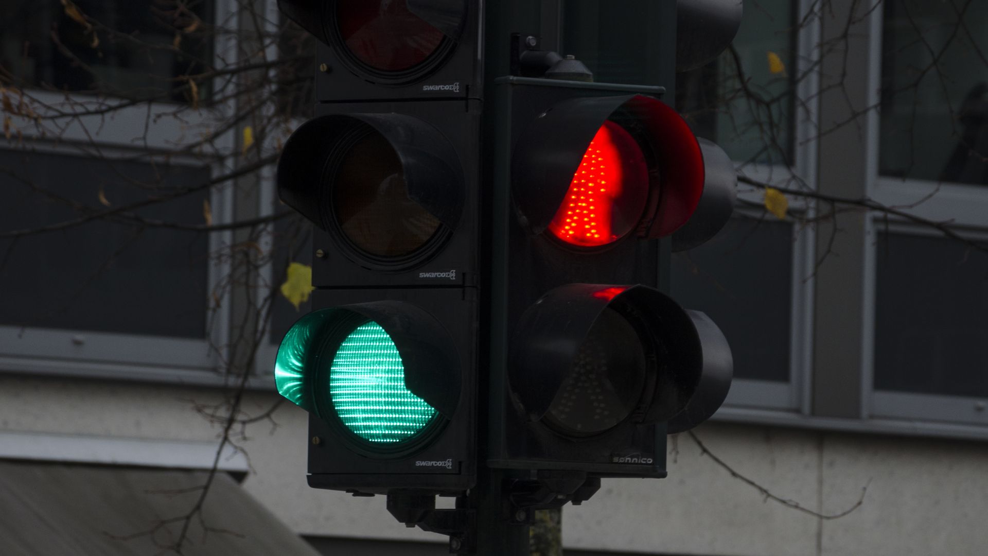Traffic light showing a bright red stop signal and a green turn arrow illuminated at the same time against an urban backdrop.