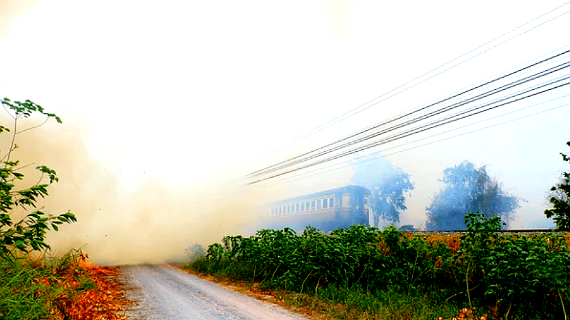 A dramatic shot of a long passenger train partially obscured by a massive cloud of thick.