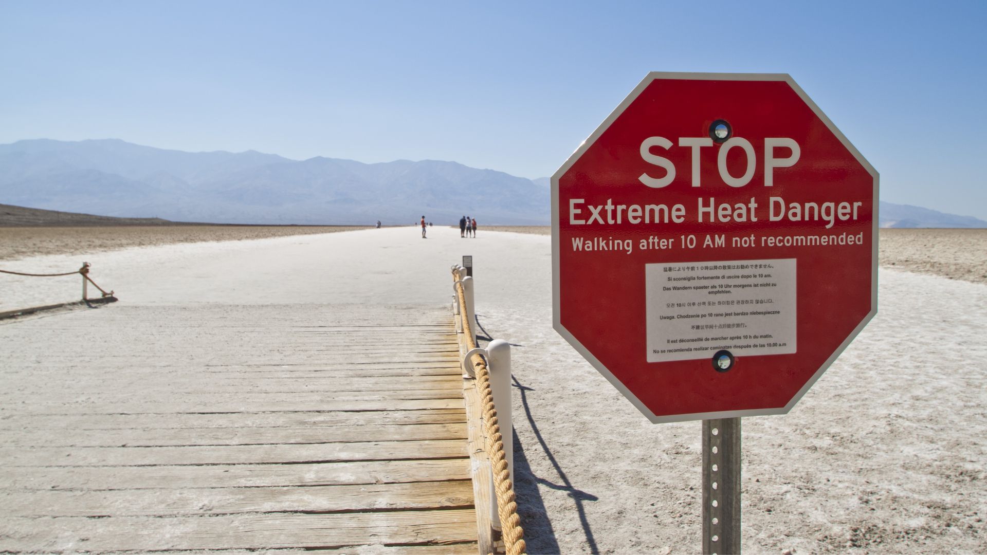 Stop sign warning of extreme heat danger along a desert boardwalk with mountains in the distance.