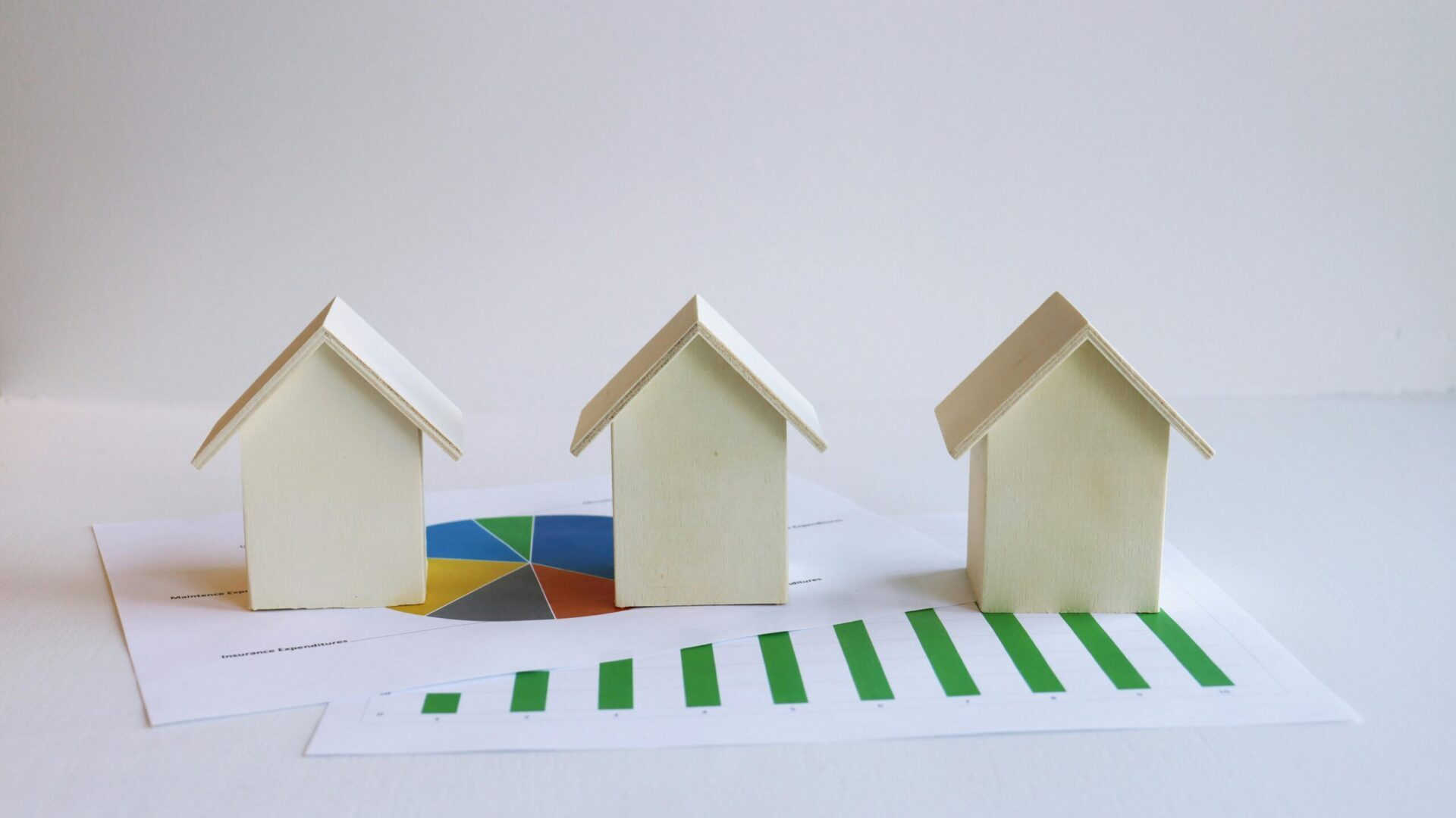 Small model houses aligned beside a rising green bar chart on a white background.