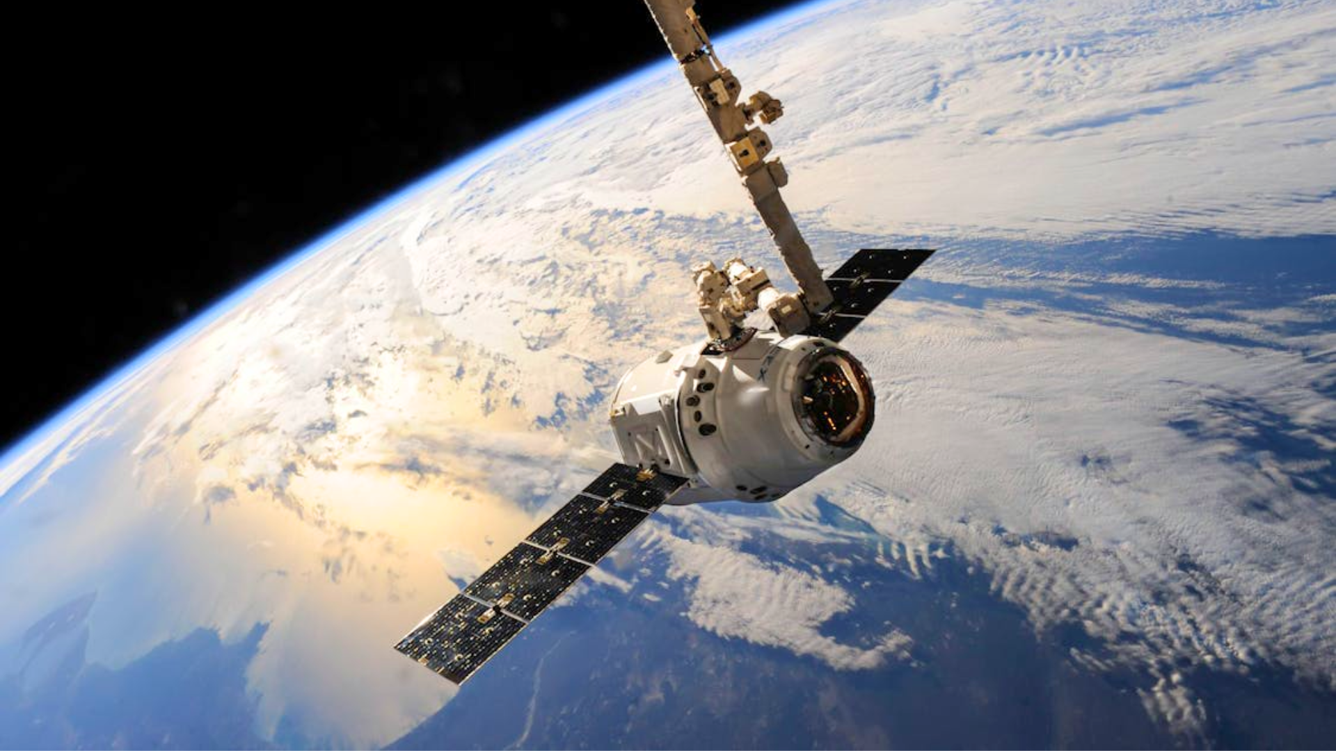 A white spacecraft with solar panels orbits high above the Earth's clouds and oceans.