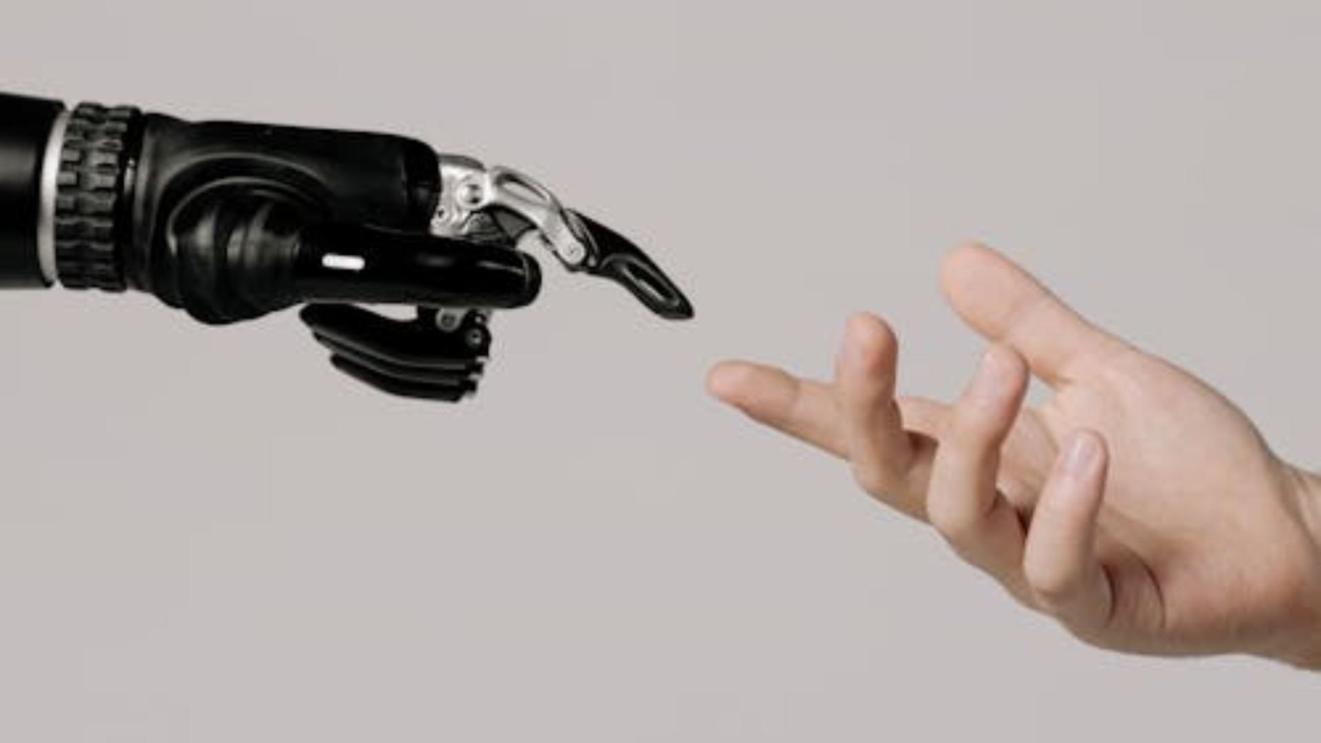 A mechanical robot hand and a human hand reach toward each other to touch fingertips.