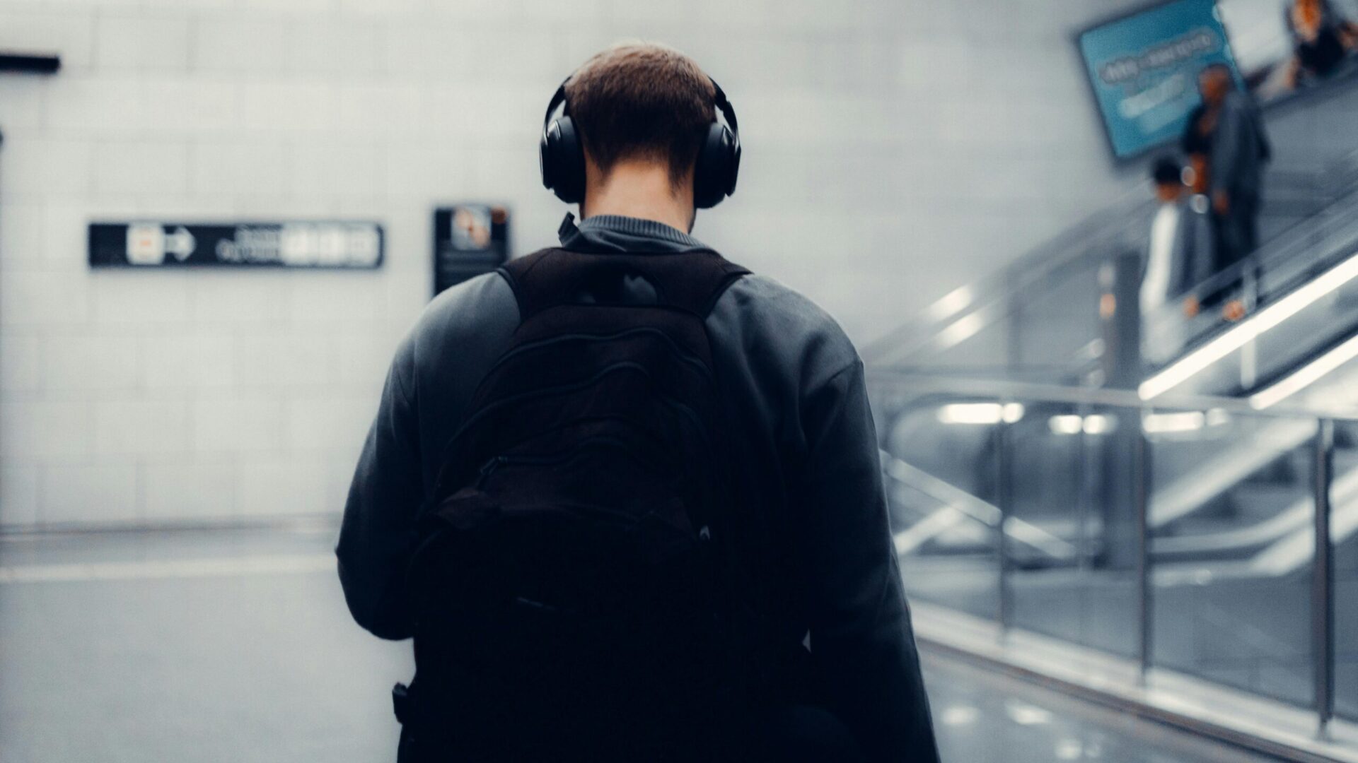 Person wearing headphones walking through a transit station corridor.