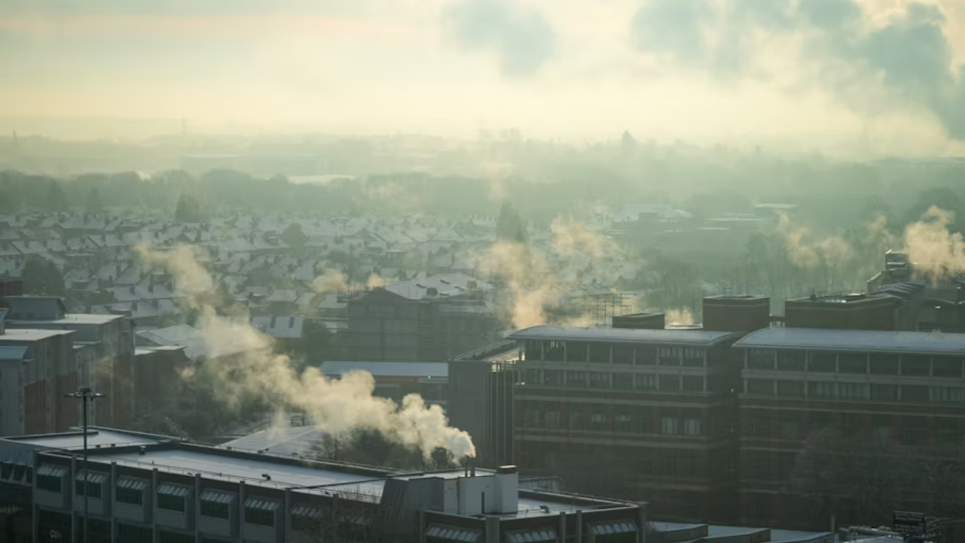 A wide city view at dawn or dusk where a low-lying layer of industrial or wildfire haze blankets a dense residential area.