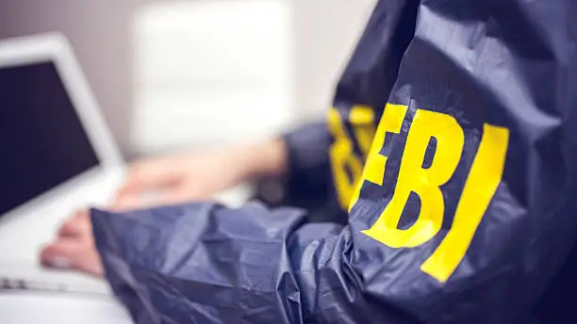 FBI jacket visible as agent uses a laptop, representing a cybercrime investigation.