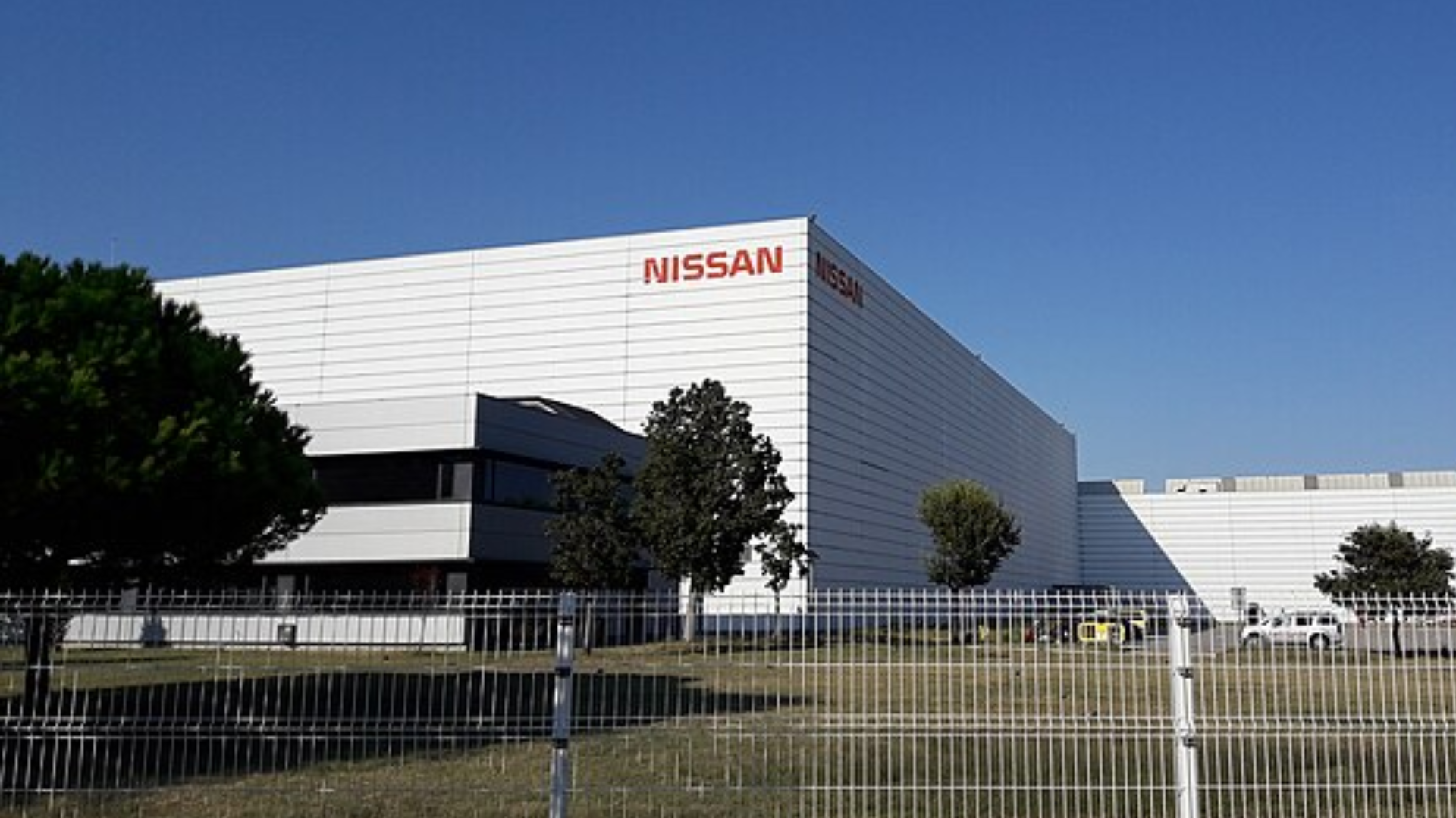 A large white factory building with the red Nissan logo on its side.