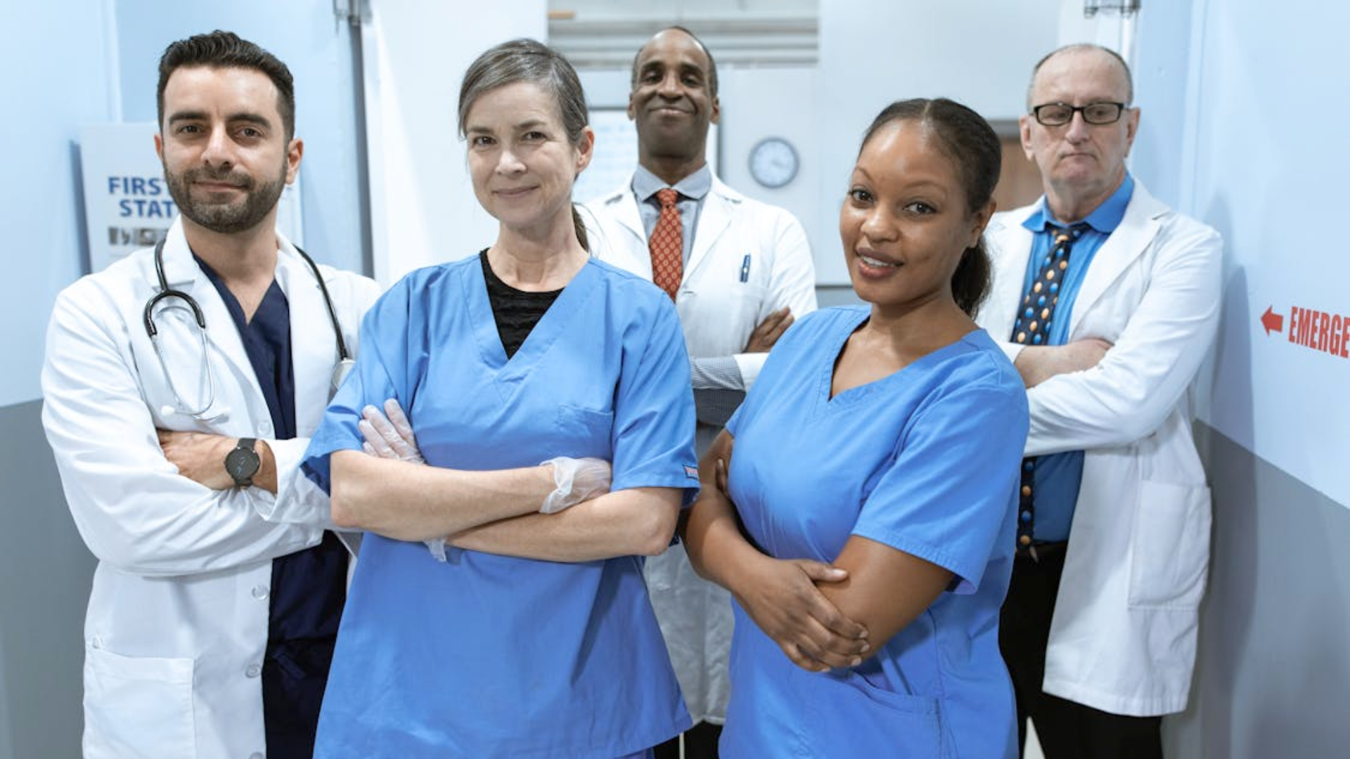 A diverse team of five doctors and nurses stand together in a hospital hallway.