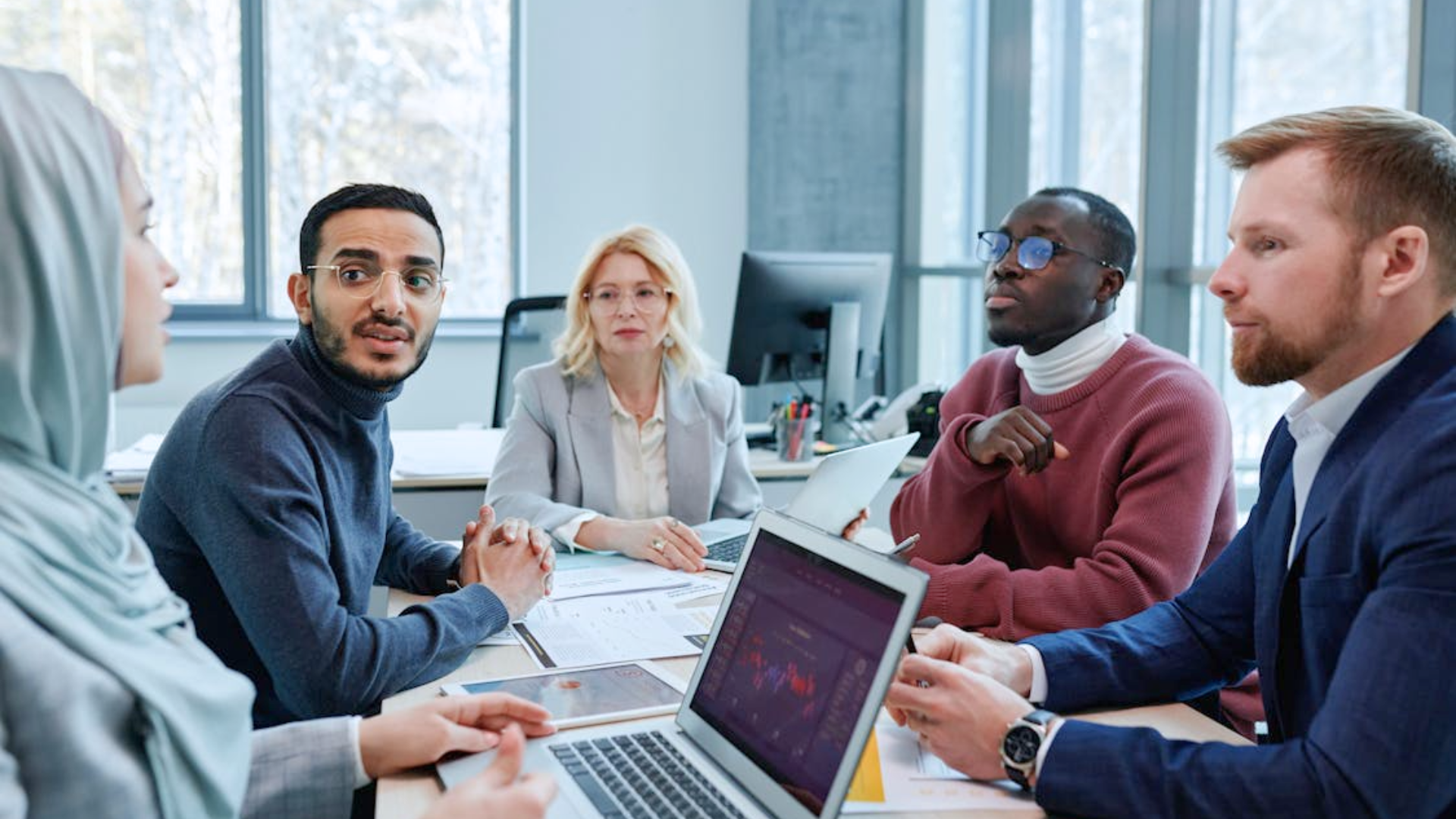 A diverse group of people sit around a table talking during a business meeting.