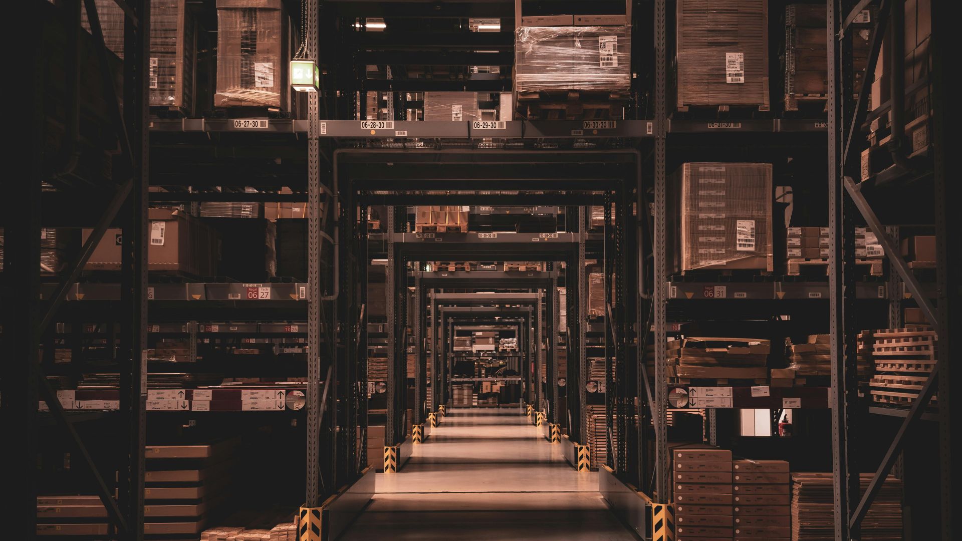 Warehouse aisle with tall shelves stacked with boxes and pallets in a distribution center.
