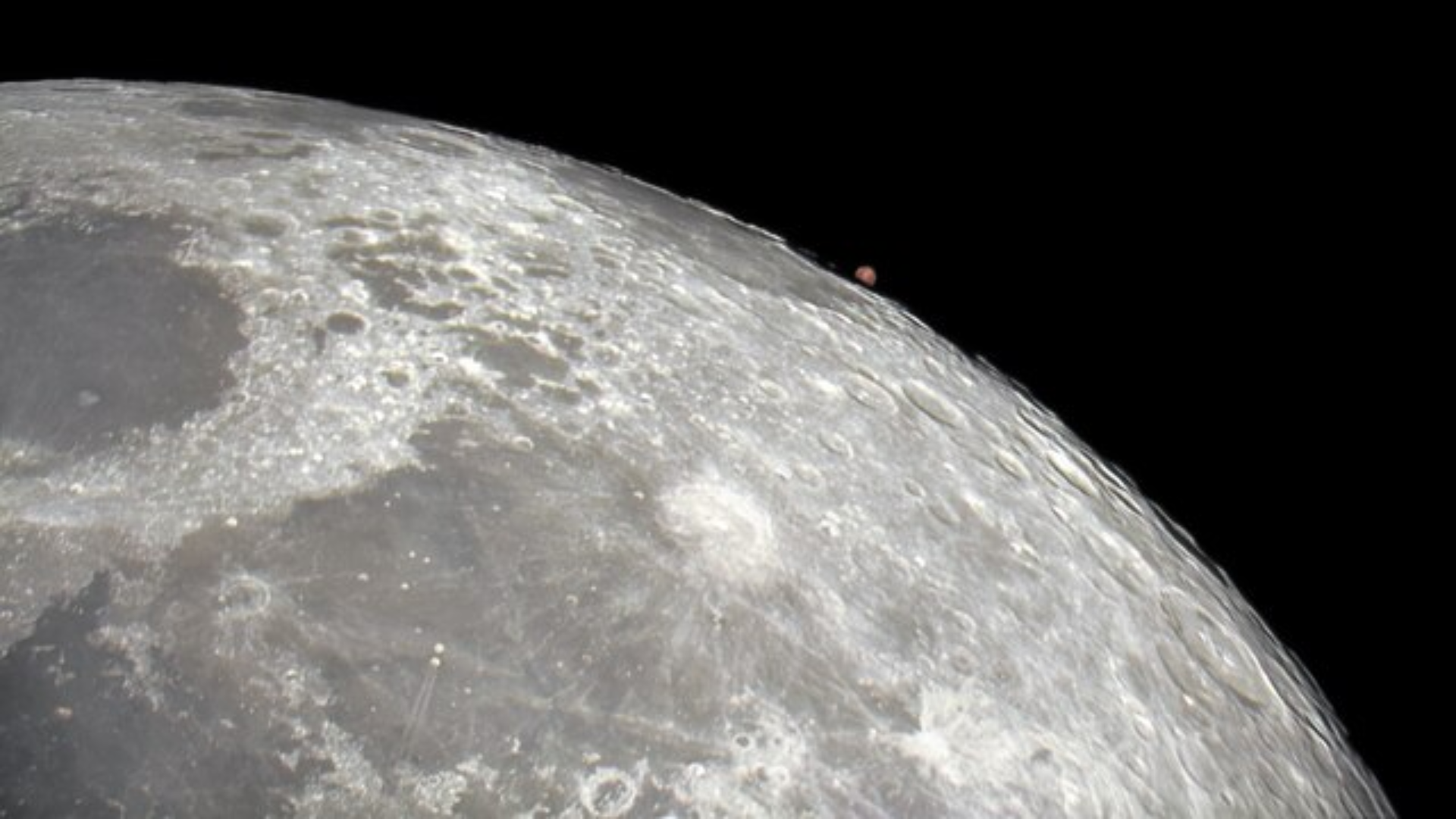 A close-up view of the Moon's cratered surface with the small, reddish planet Mars visible just above the lunar horizon.
