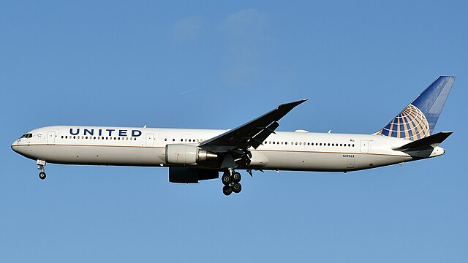A profile view of a white United Airlines Boeing 767 in mid-air against a clear blue sky.