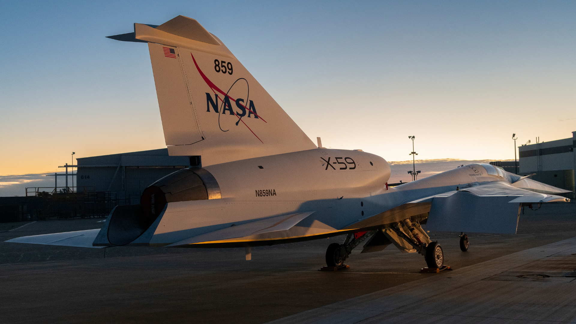 The NASA X-59 aircraft, marked with the NASA logo and _X-59_ on its tail, sits parked on an airfield ramp during the golden hour of sunset.