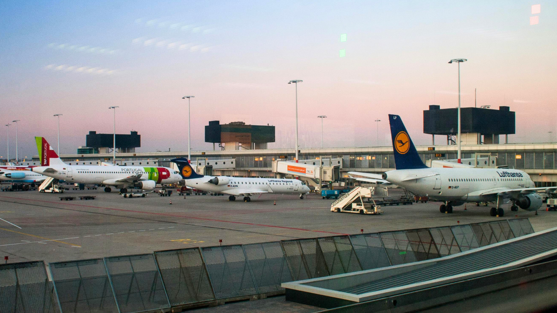 A row of commercial aircraft parked at terminal gates during a hazy sunset at an airport.
