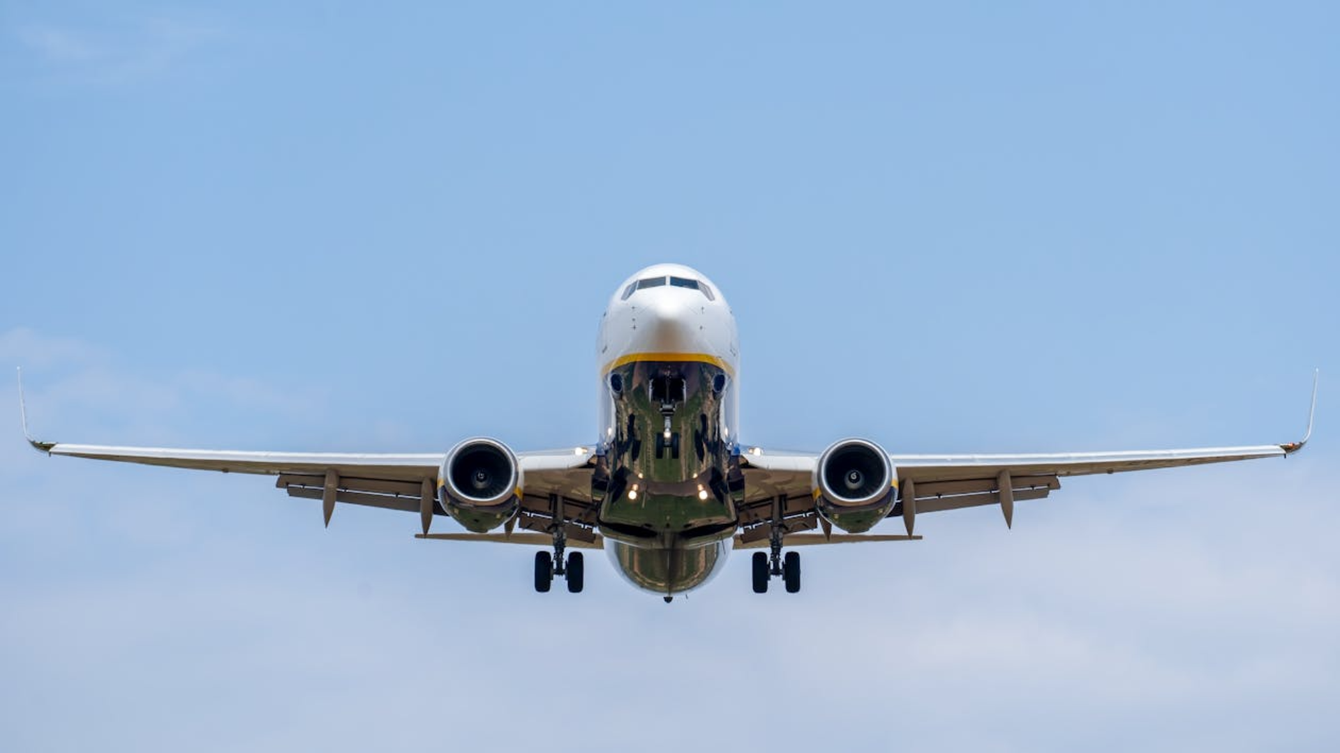 A front-facing view of a commercial jet with its landing gear down as it descends against a clear blue sky.