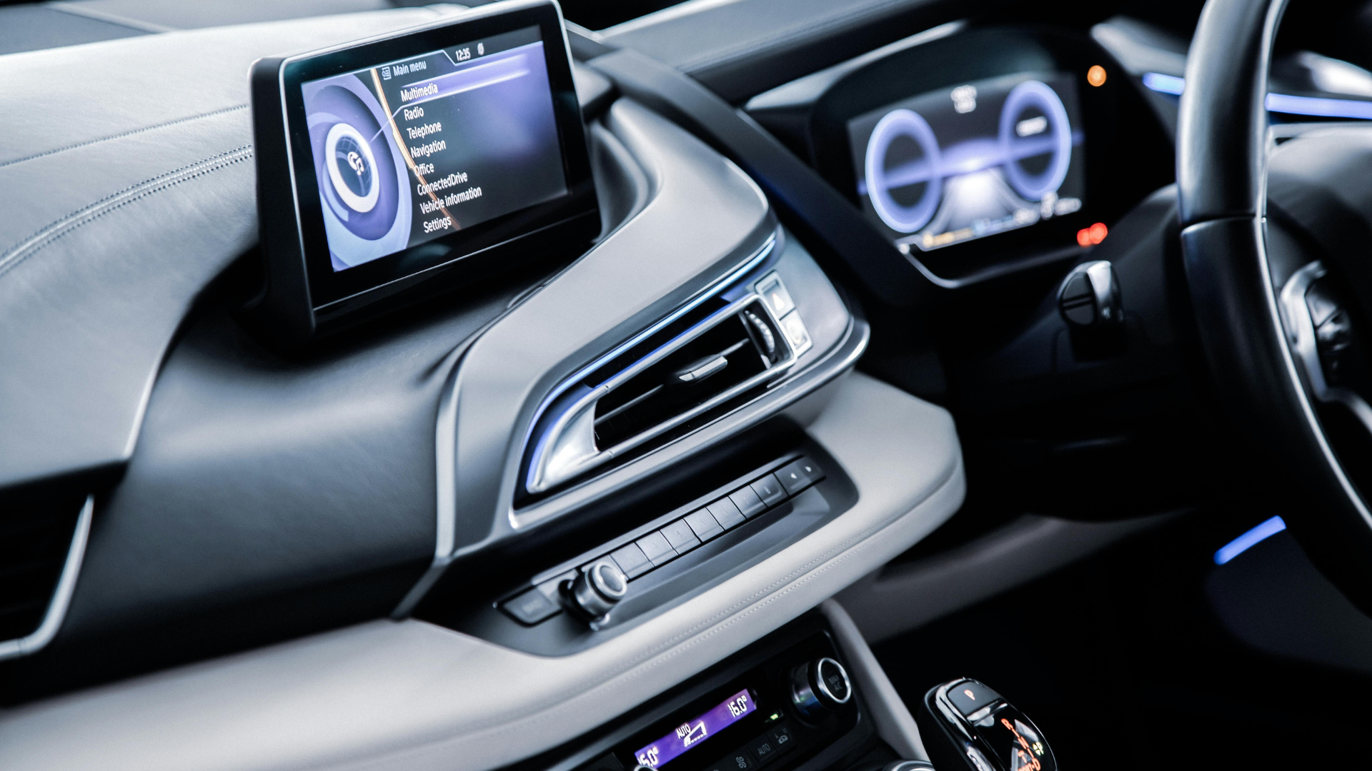The modern interior of a vehicle features a digital infotainment screen displaying a menu next to a glowing blue instrument cluster and sleek dashboard vents.