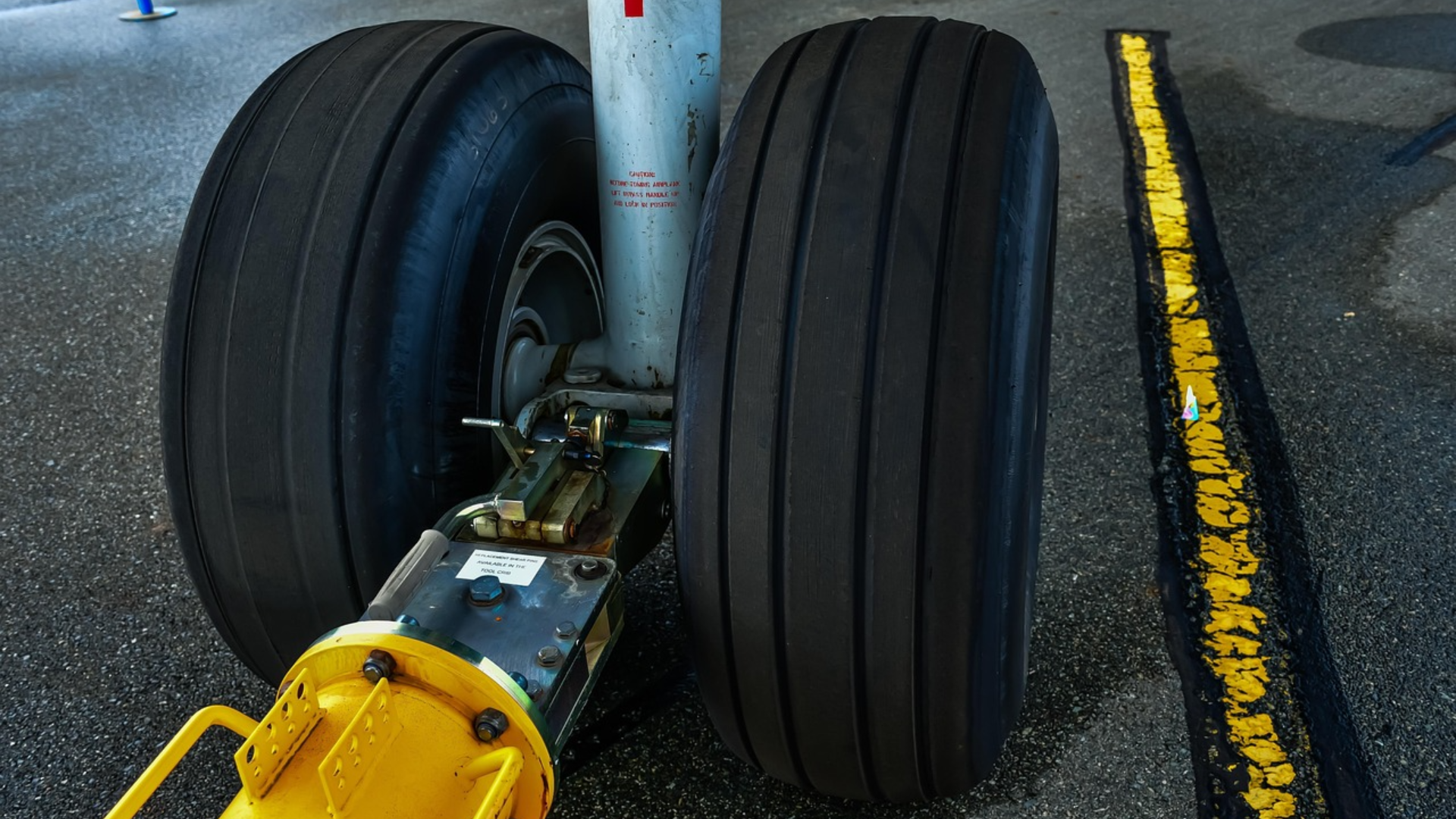 A close-up of an airplane's nose landing gear with a yellow tow bar attached to the wheel assembly on the tarmac.