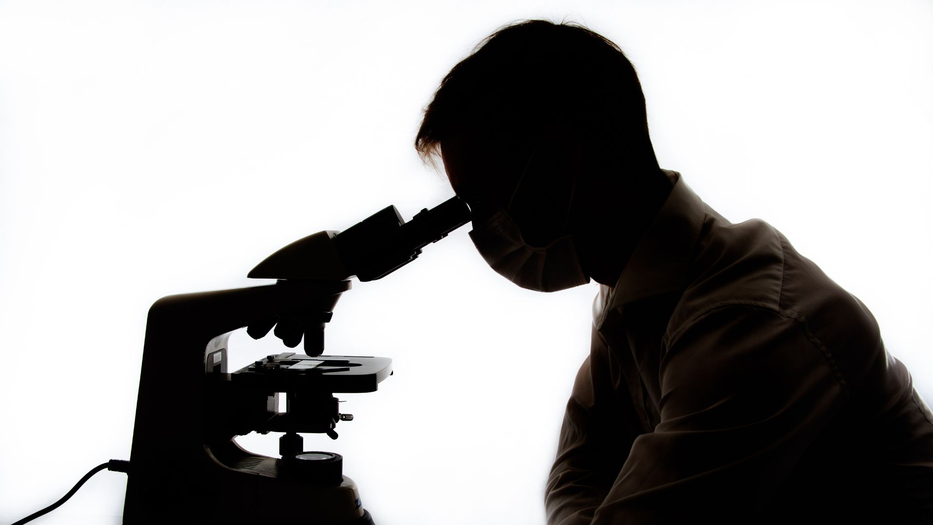 Silhouette of a scientist looking through a microscope against a white background.