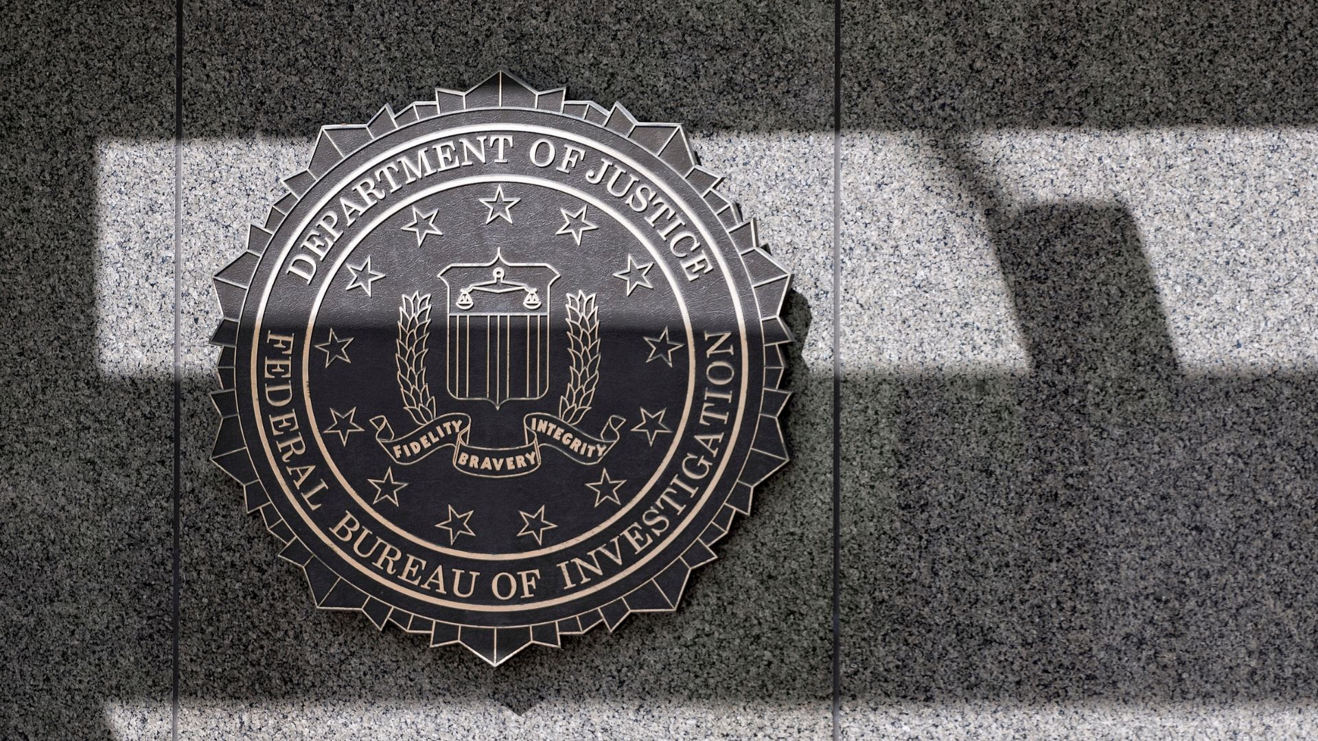 Federal Bureau of Investigation seal mounted on granite wall with dramatic shadow.
