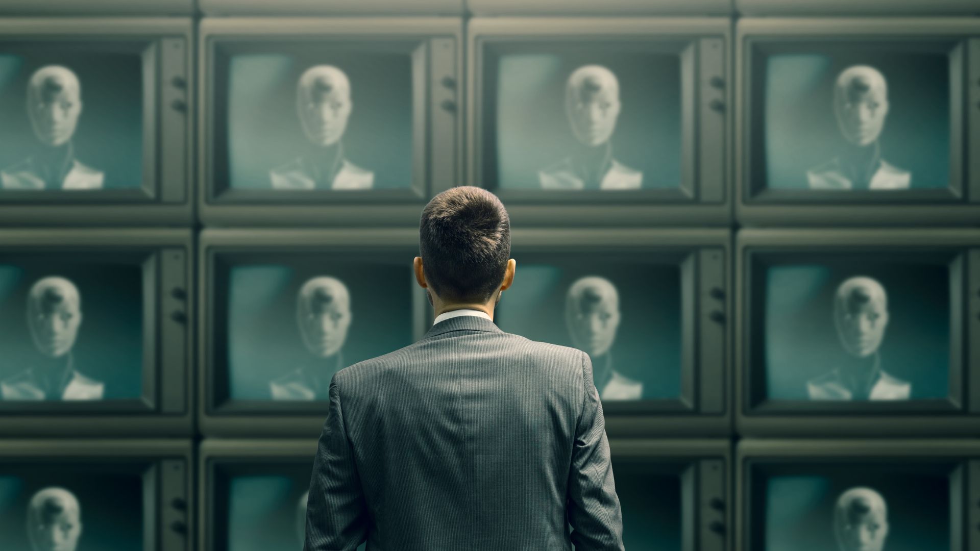 A man in a suit stands facing a wall of vintage TVs, each displaying a humanoid AI robot face.