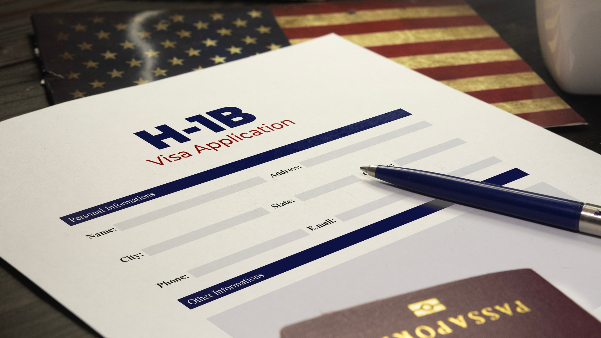 A close-up of an H-1B visa application form on a wooden desk next to a pen, a passport, and a small American flag.