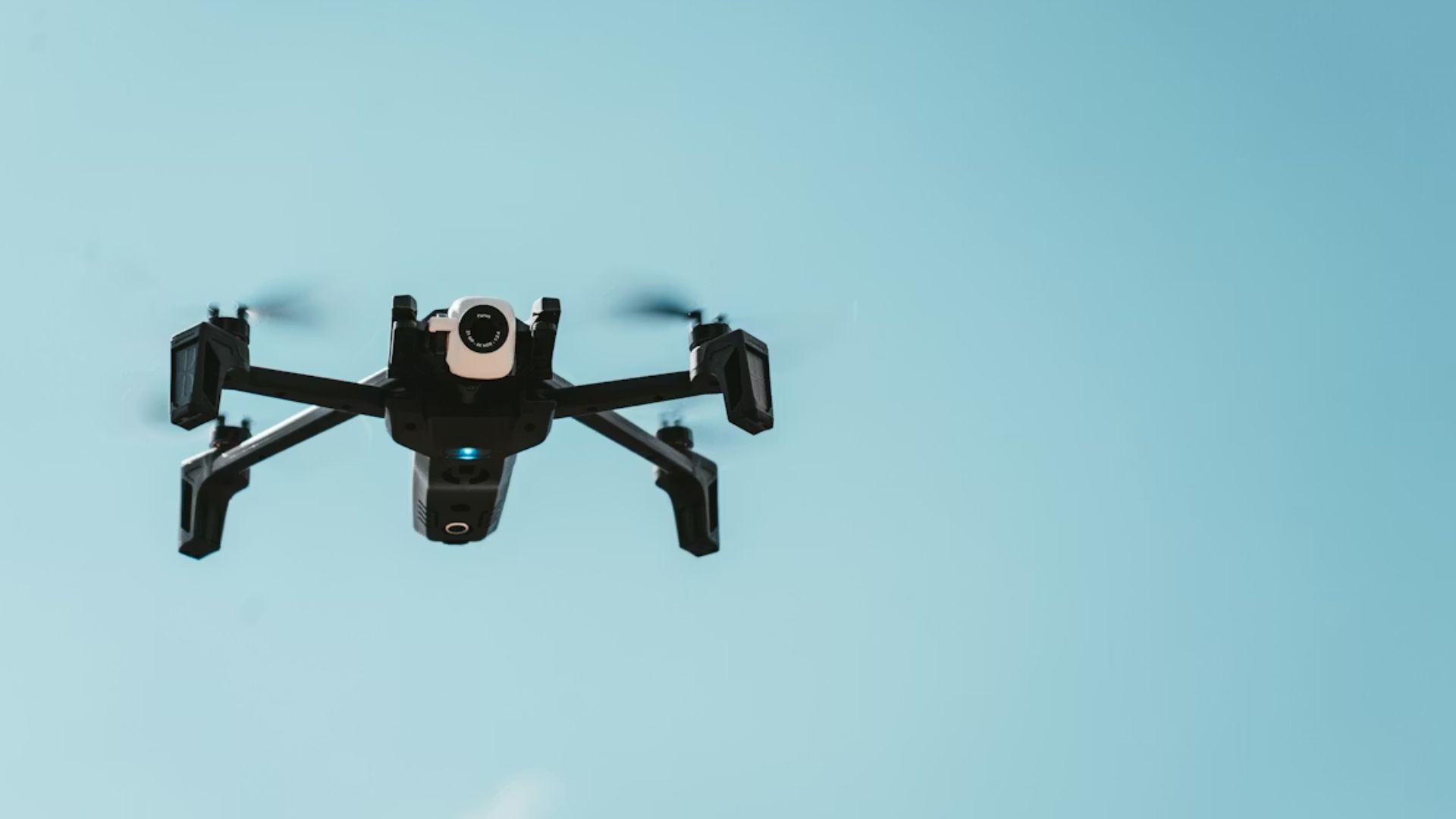 Close up on a black quadcopter drone in flight against a clear blue sky.