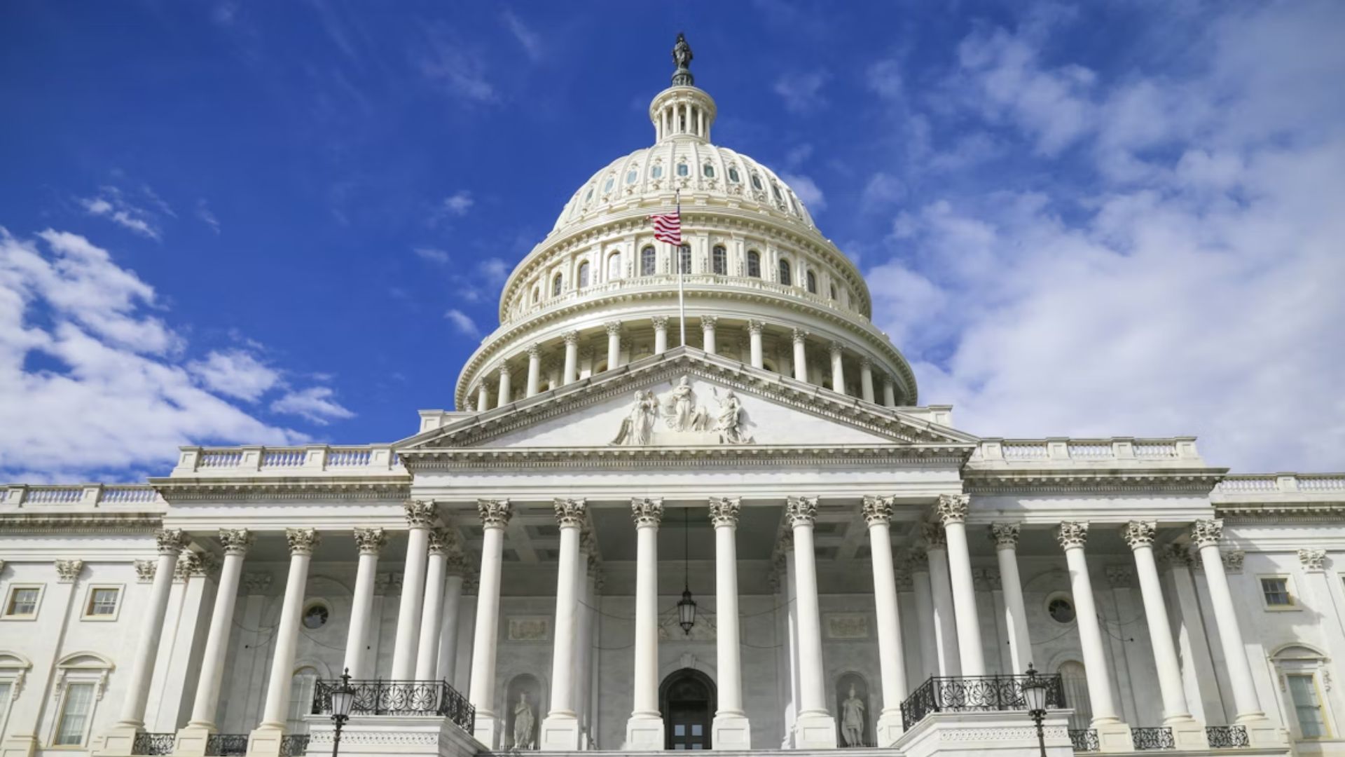 United States Capitol building facade with American flag against blue sky.