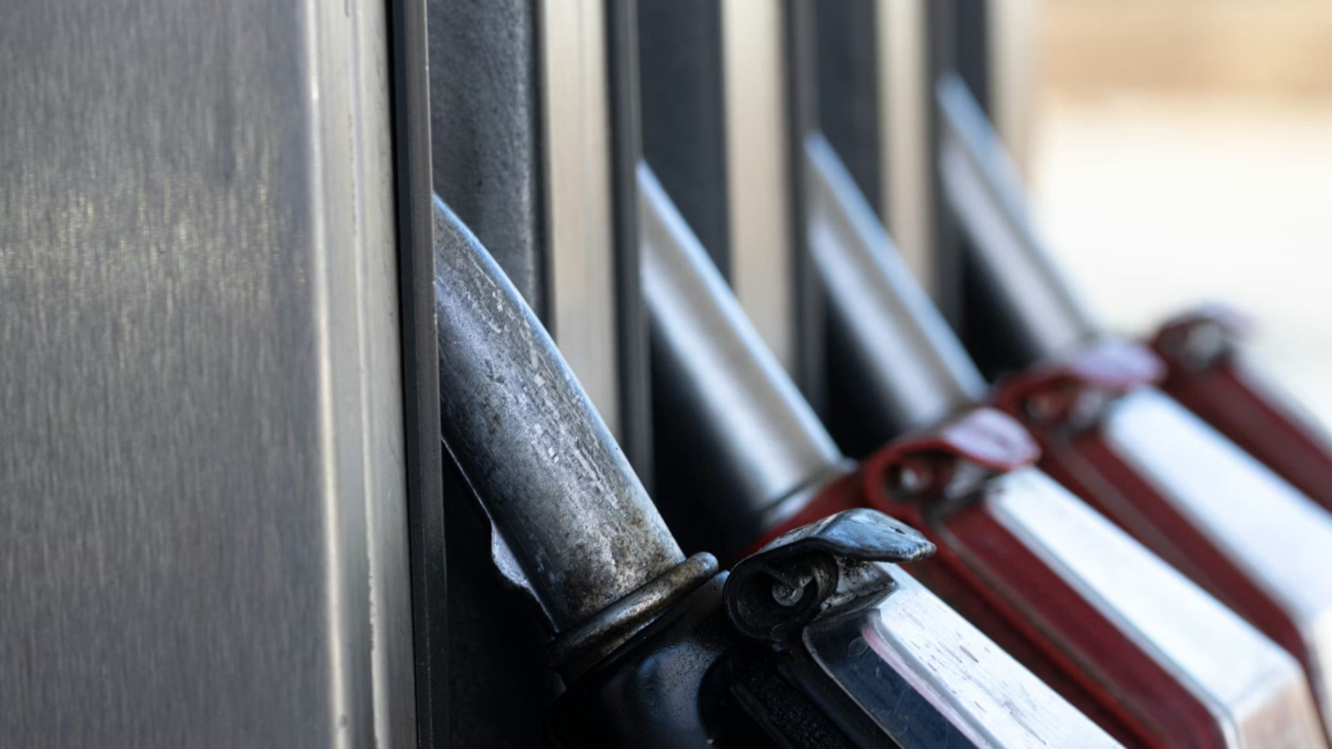 A close-up of several metallic fuel nozzles hanging at a gas station pump.