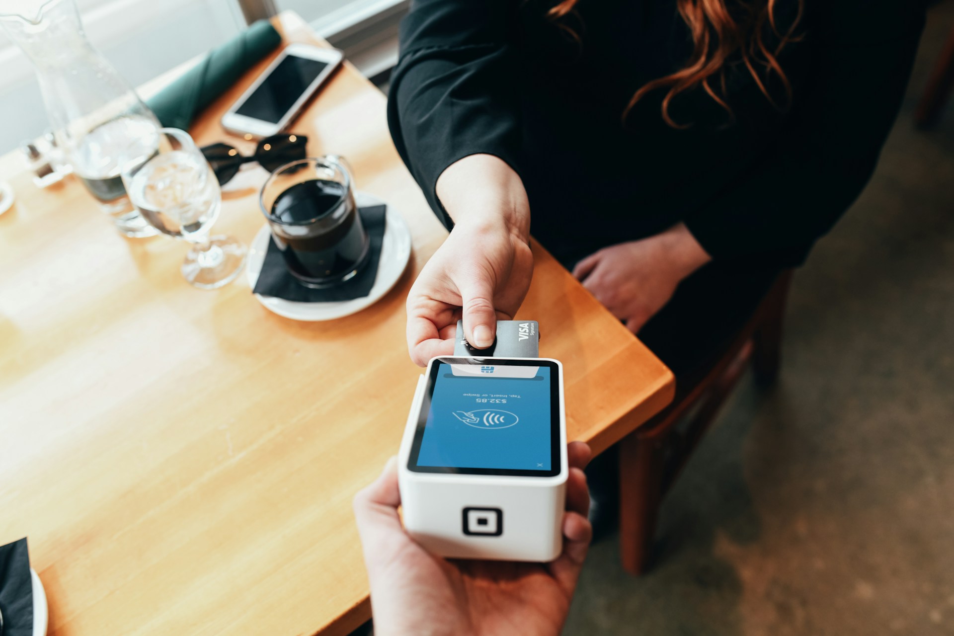 Person making contactless payment with card at table in cafe setting.