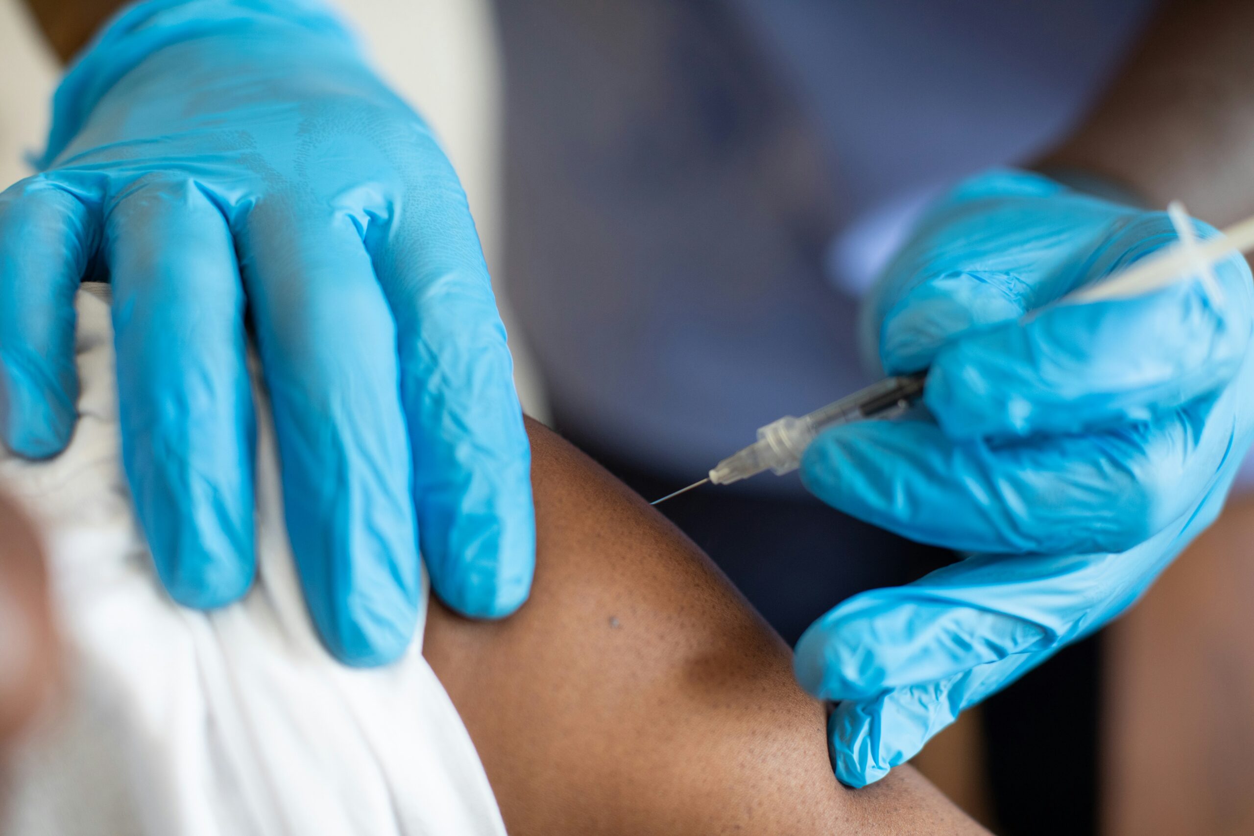 Medical worker wearing blue gloves administering an injection into a patient’s upper arm.