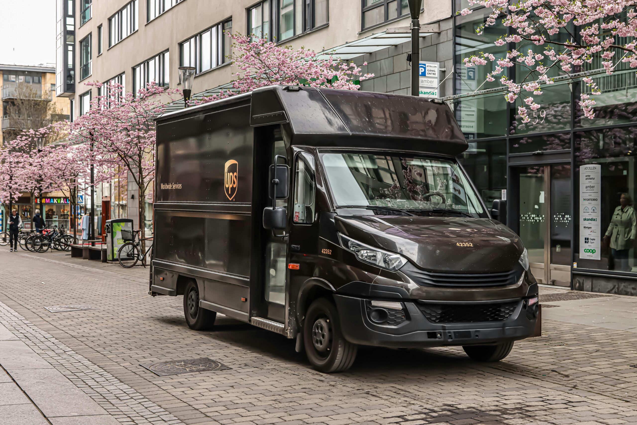 UPS delivery truck parked on a city street lined with blooming trees and storefronts.