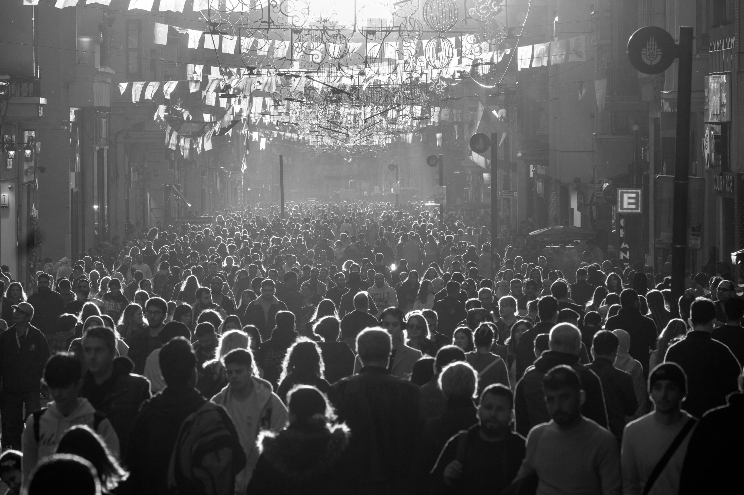 Dense crowd of people walking down a decorated city street in black and white.