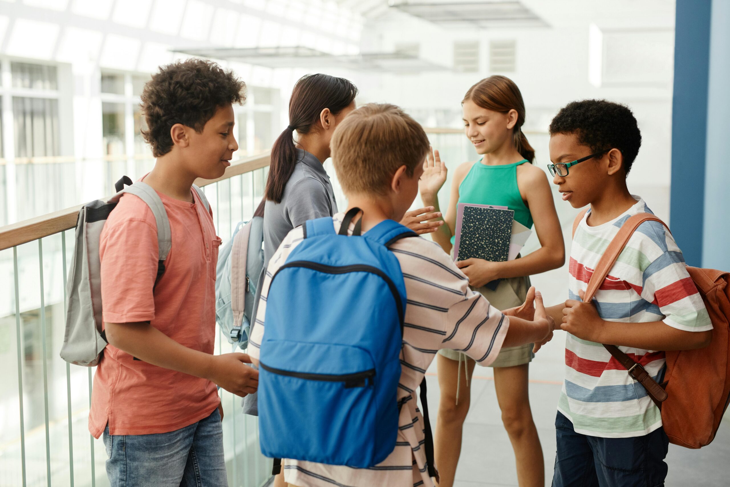 Group of schoolchildren with backpacks greeting each other in a hallway.