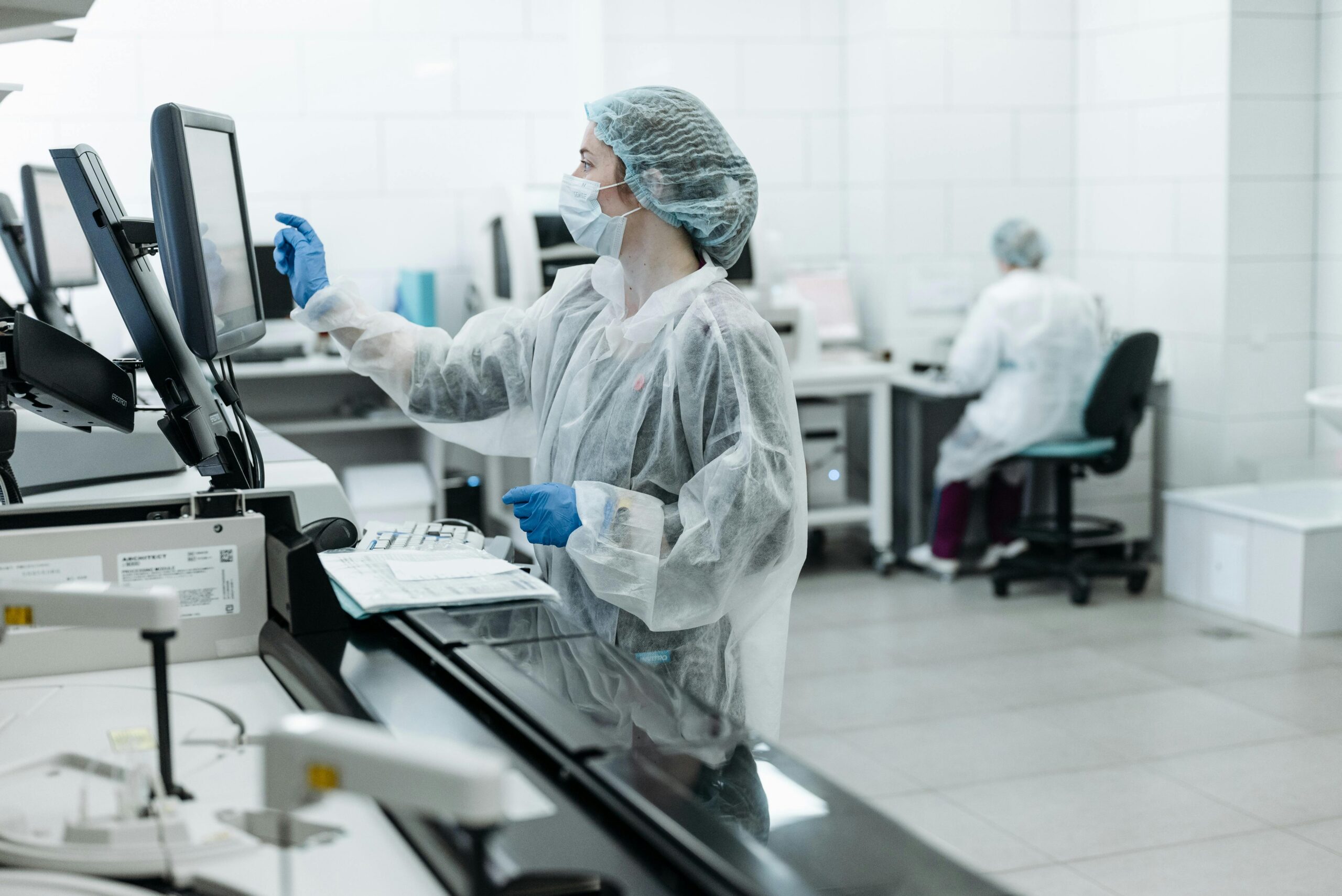 Lab technician in protective gear operating medical testing equipment in a clinical laboratory.