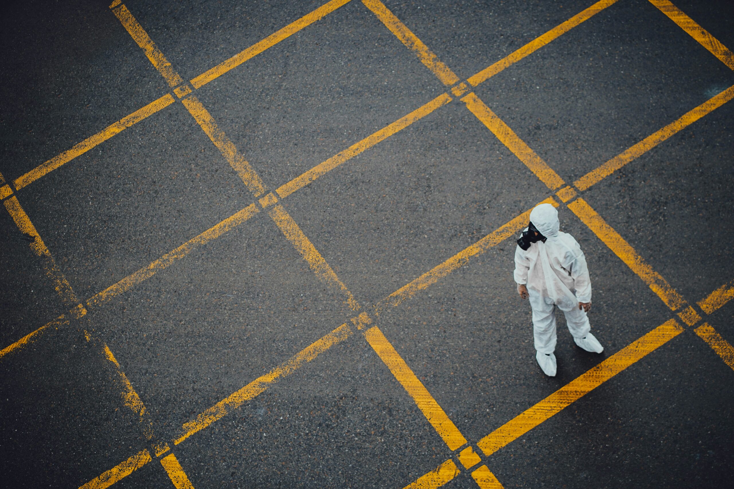 Person in a white hazmat suit standing alone on a road marked with yellow crosshatch lines.