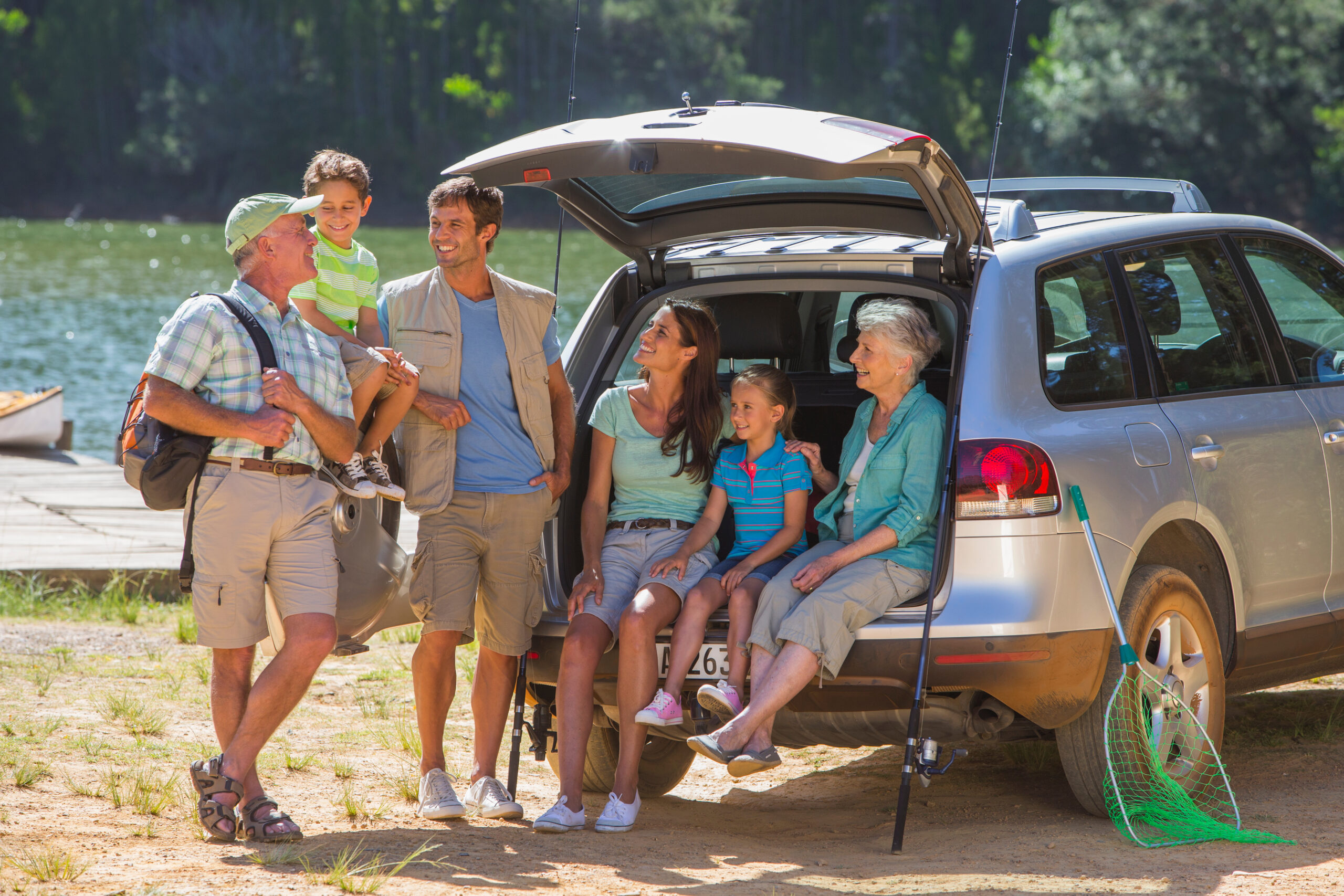 Family gathered by an SUV at a lakeside.