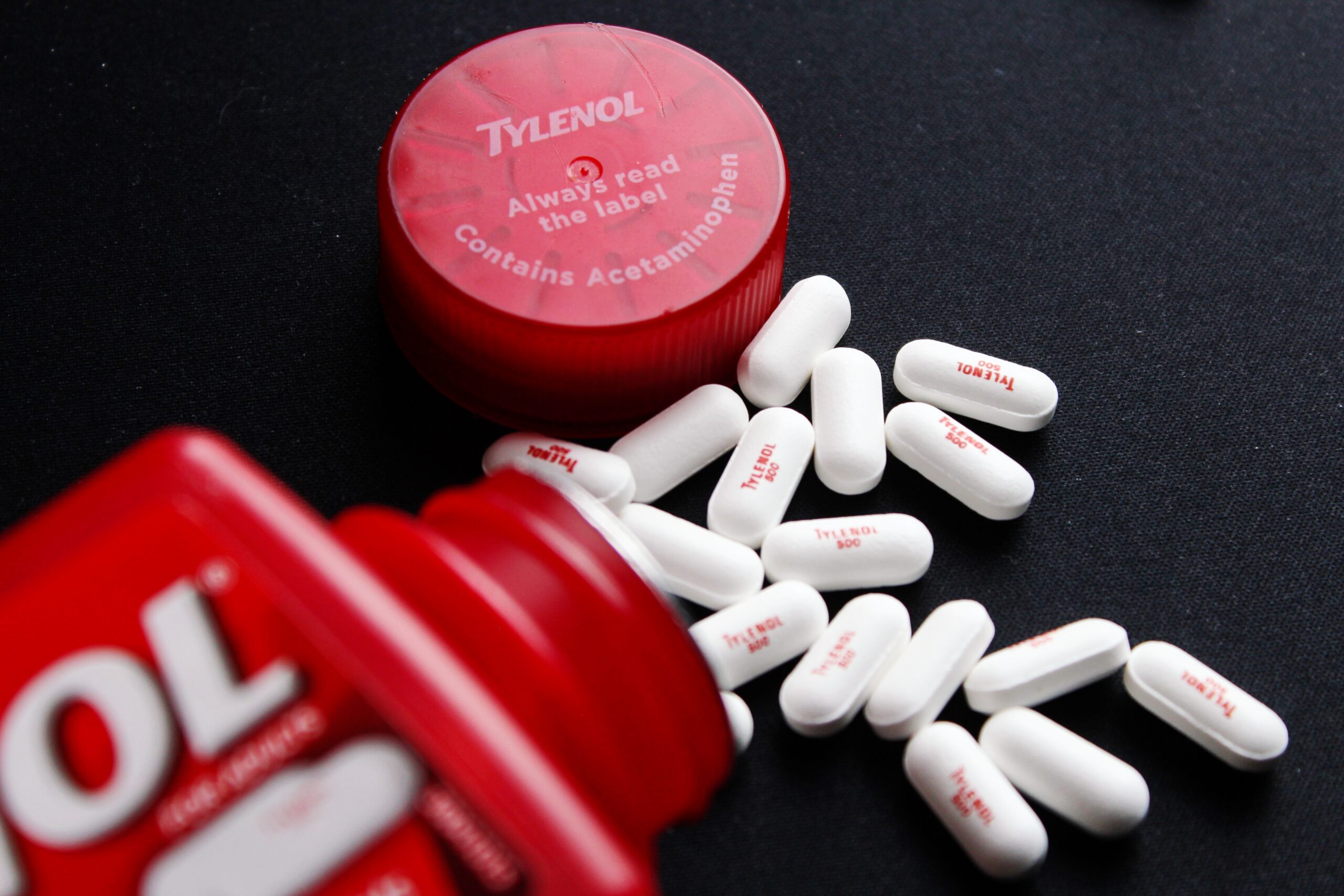 Tylenol bottle and white tablets scattered on a dark surface.